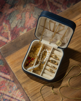 Open jewelry box with beige interior containing multiple gold chains and pendants