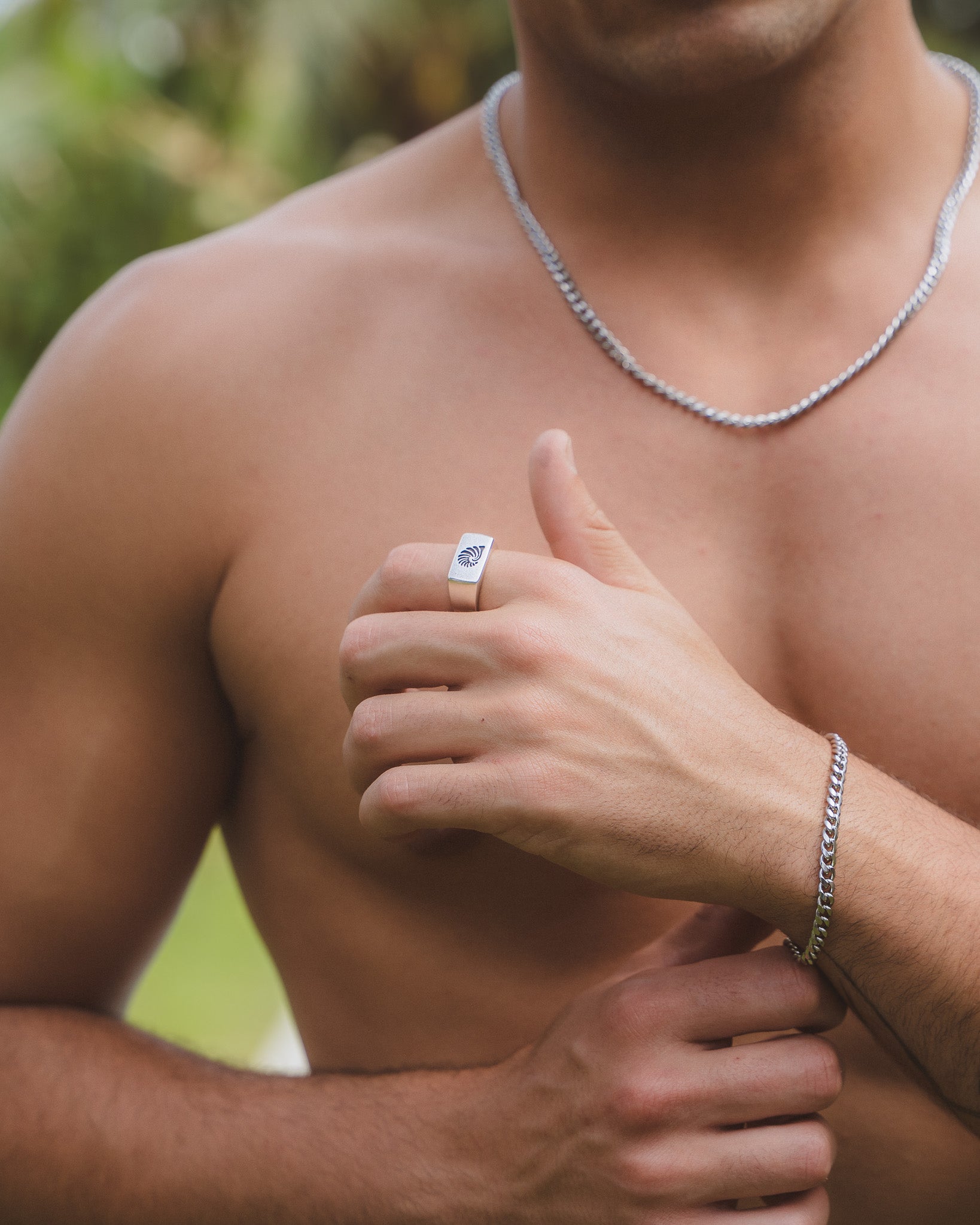 Man wearing a square-faced silver shell ring on his finger and a silver chain necklace.