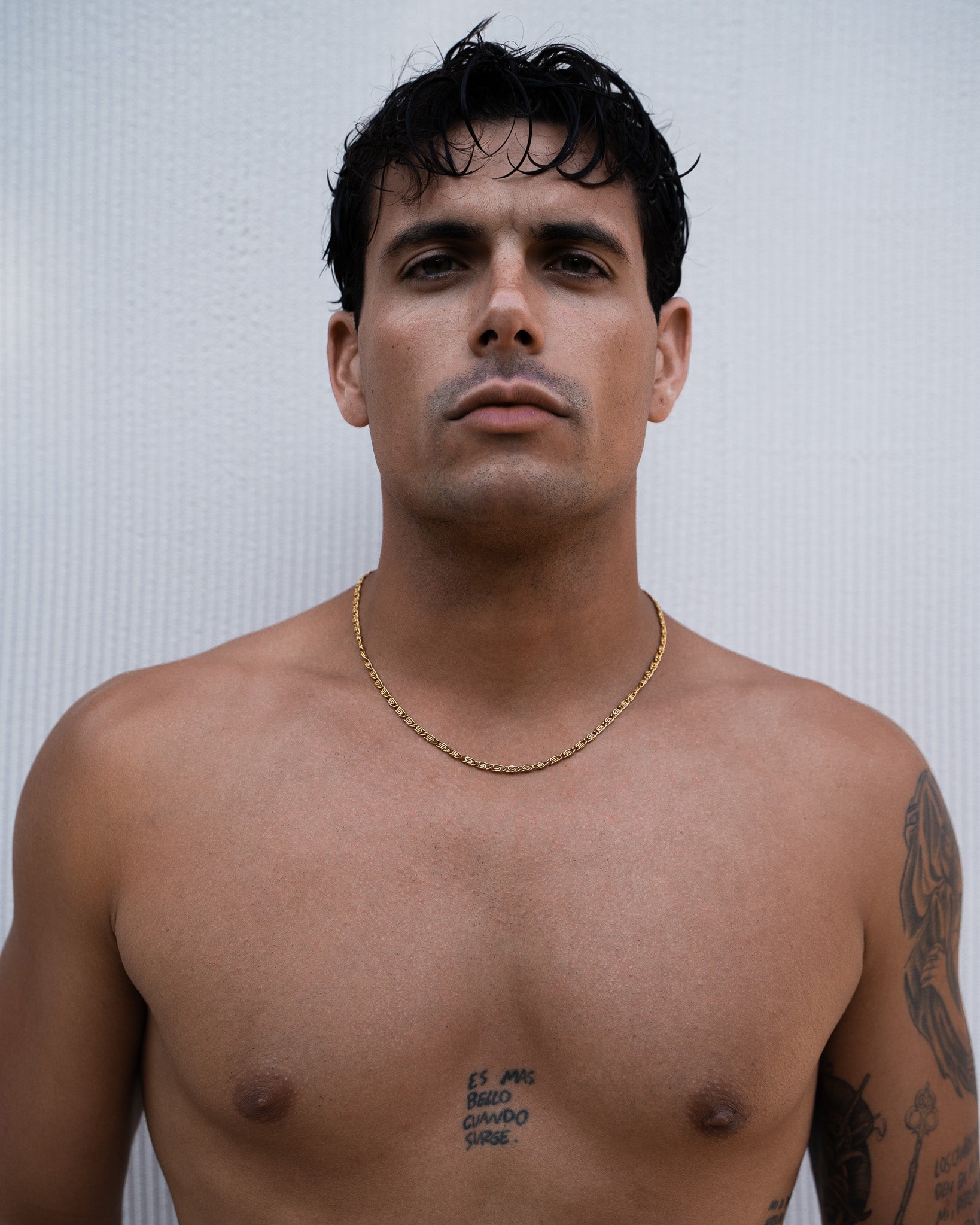 Close up of a man wearing a 4 mm gold NUSA chain necklace against a light textured background.