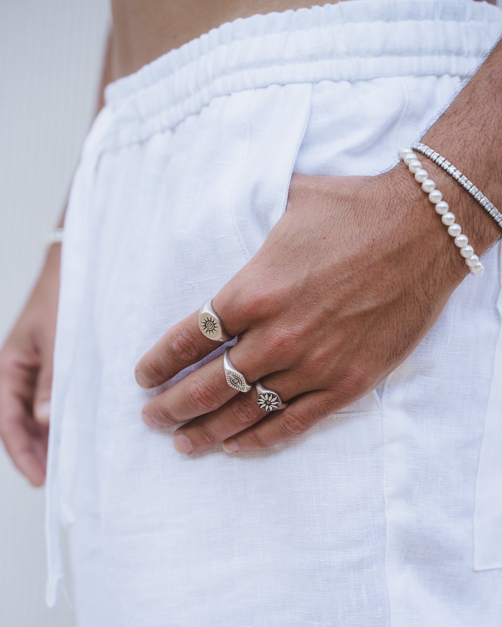 Side view of a man wearing ENERGY SILVER RINGS with a pearl bracelet and a crystal bracelet.