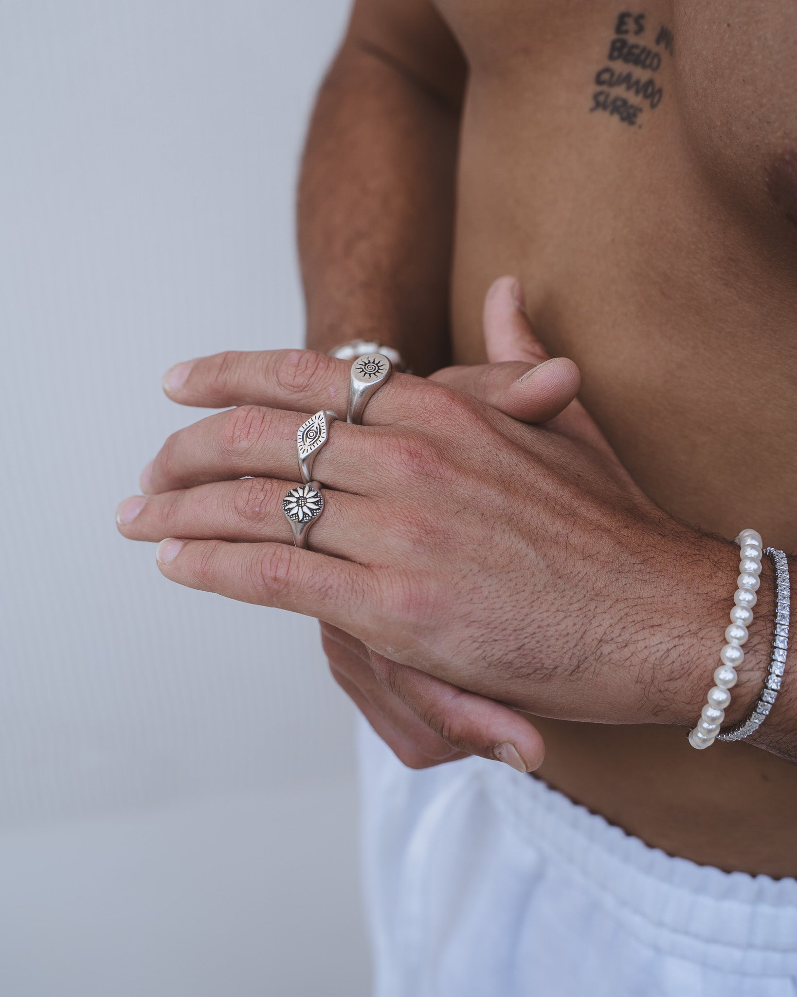 Close up of a hand wearing ENERGY SILVER RING with sun motif on finger and a tattooed chest in background.