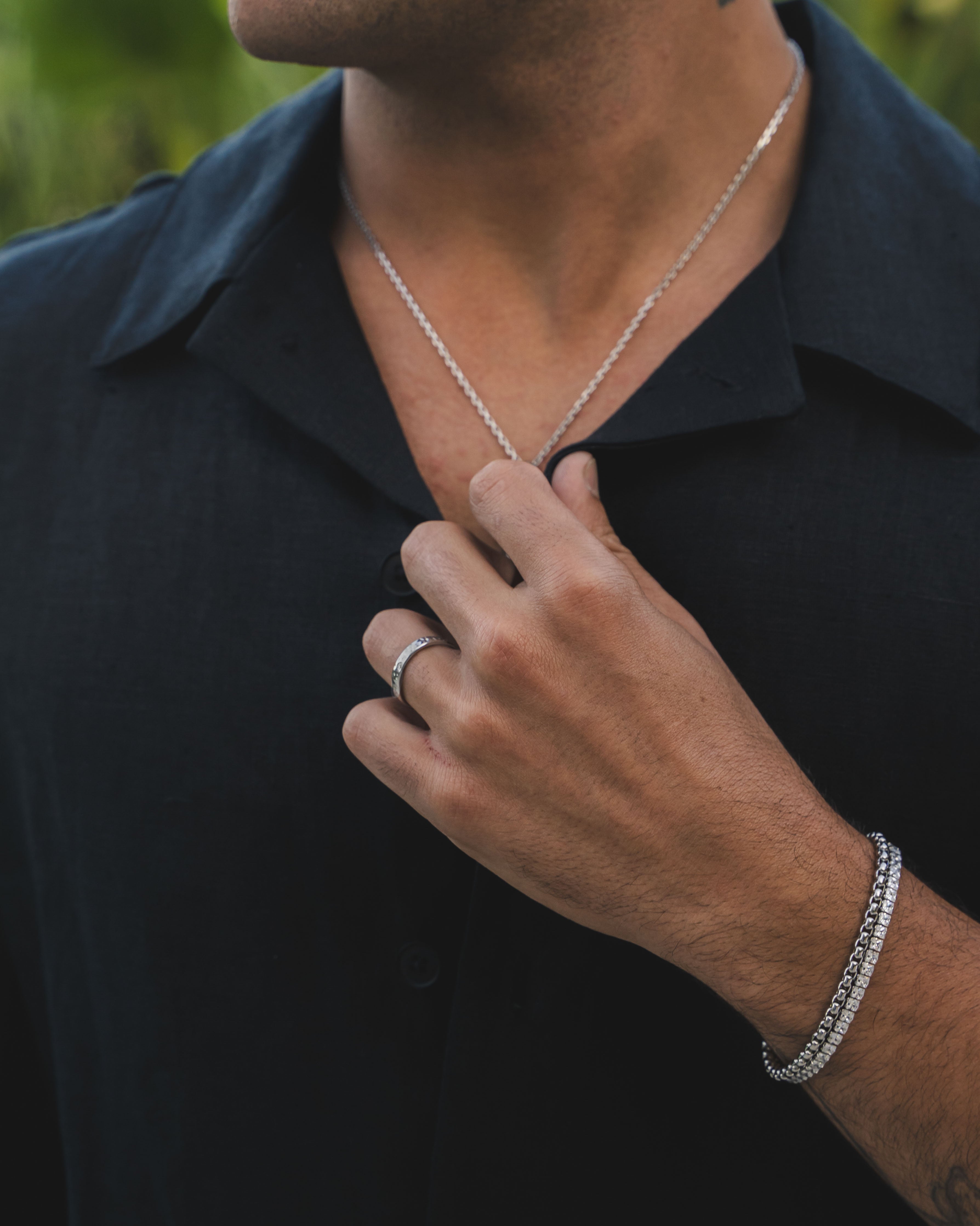 Hammered silver ring on a man's finger with a silver chain necklace visible in the background