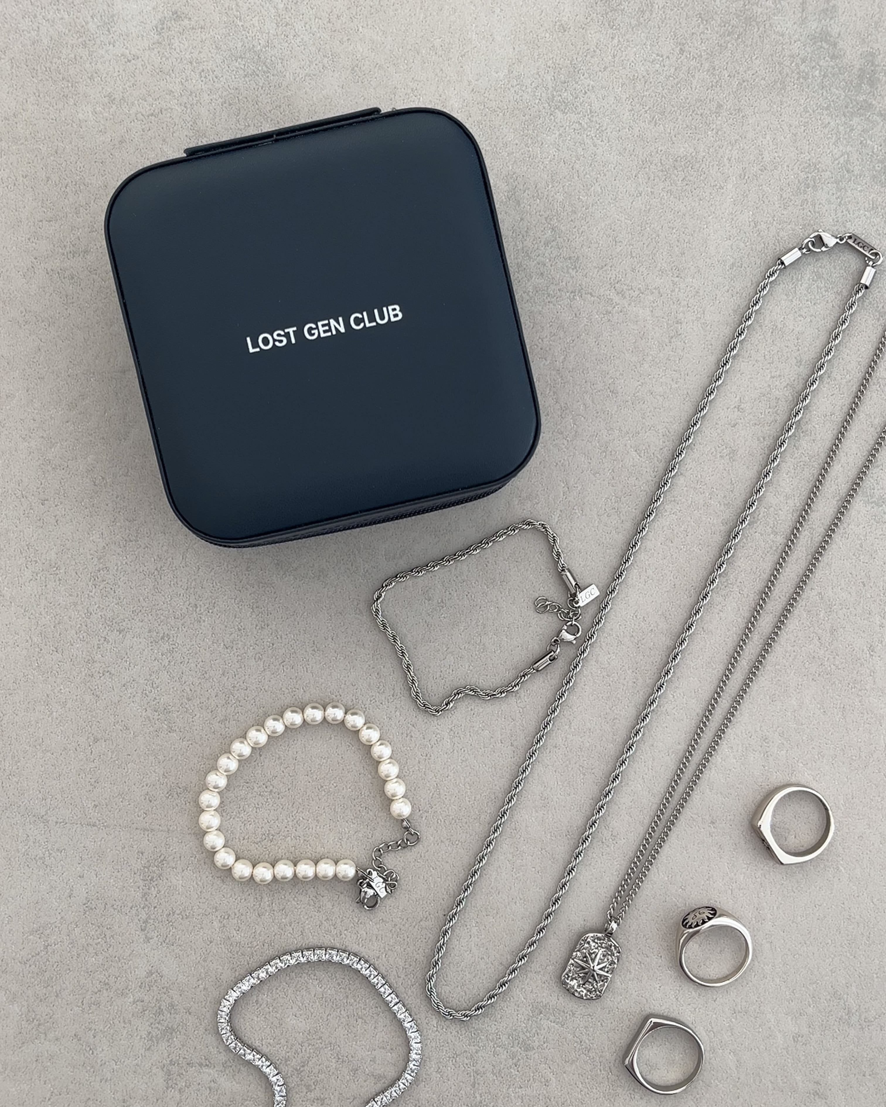 Beige travel jewelry box open with multiple gold necklaces rings and a pearl bracelet arranged in sections.