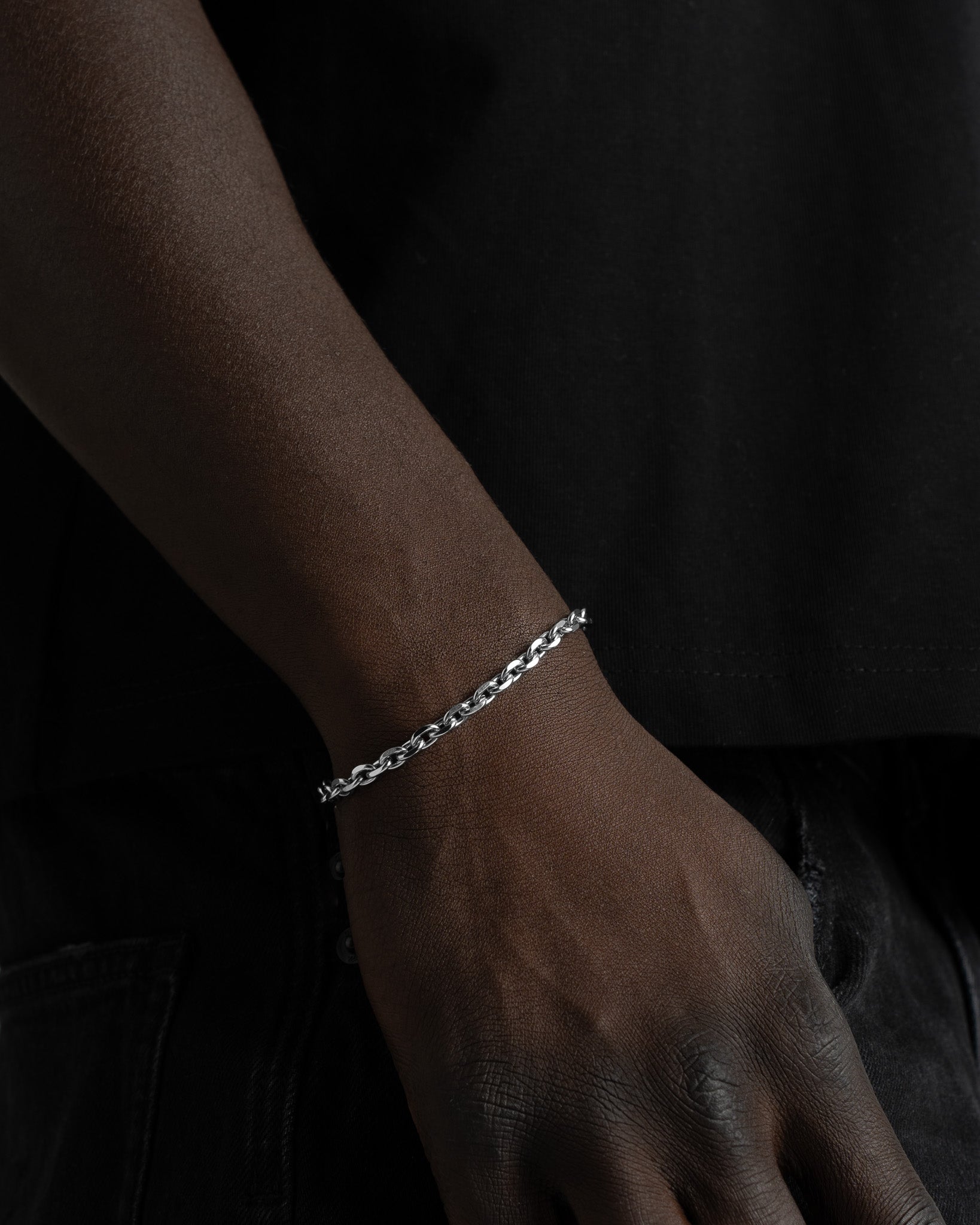 Close-up of a silver anchor bracelet on a dark-skinned wrist against a black background