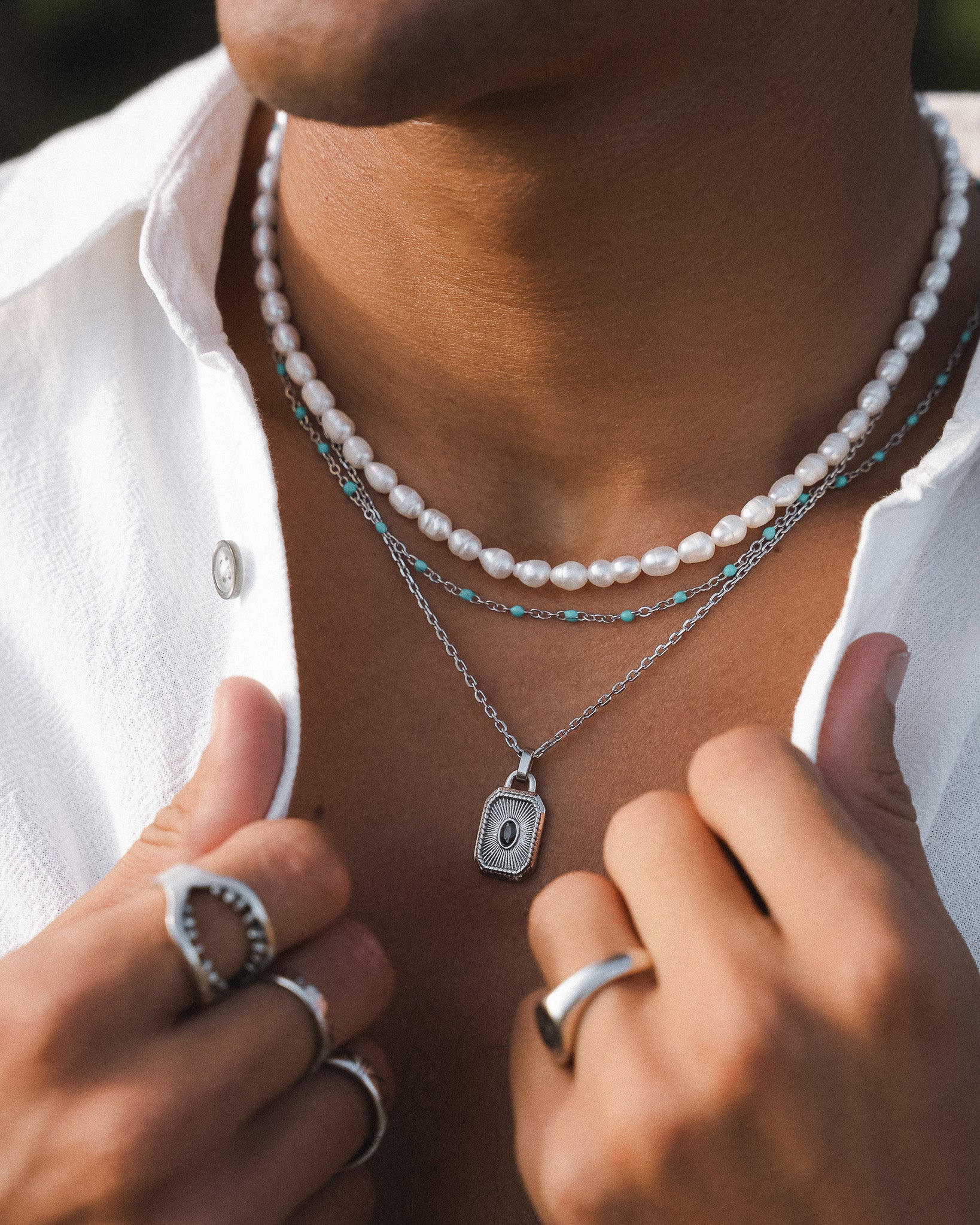Layered necklace featuring a white pearl strand turquoise beads and an ornate rectangular pendant on a silver chain.