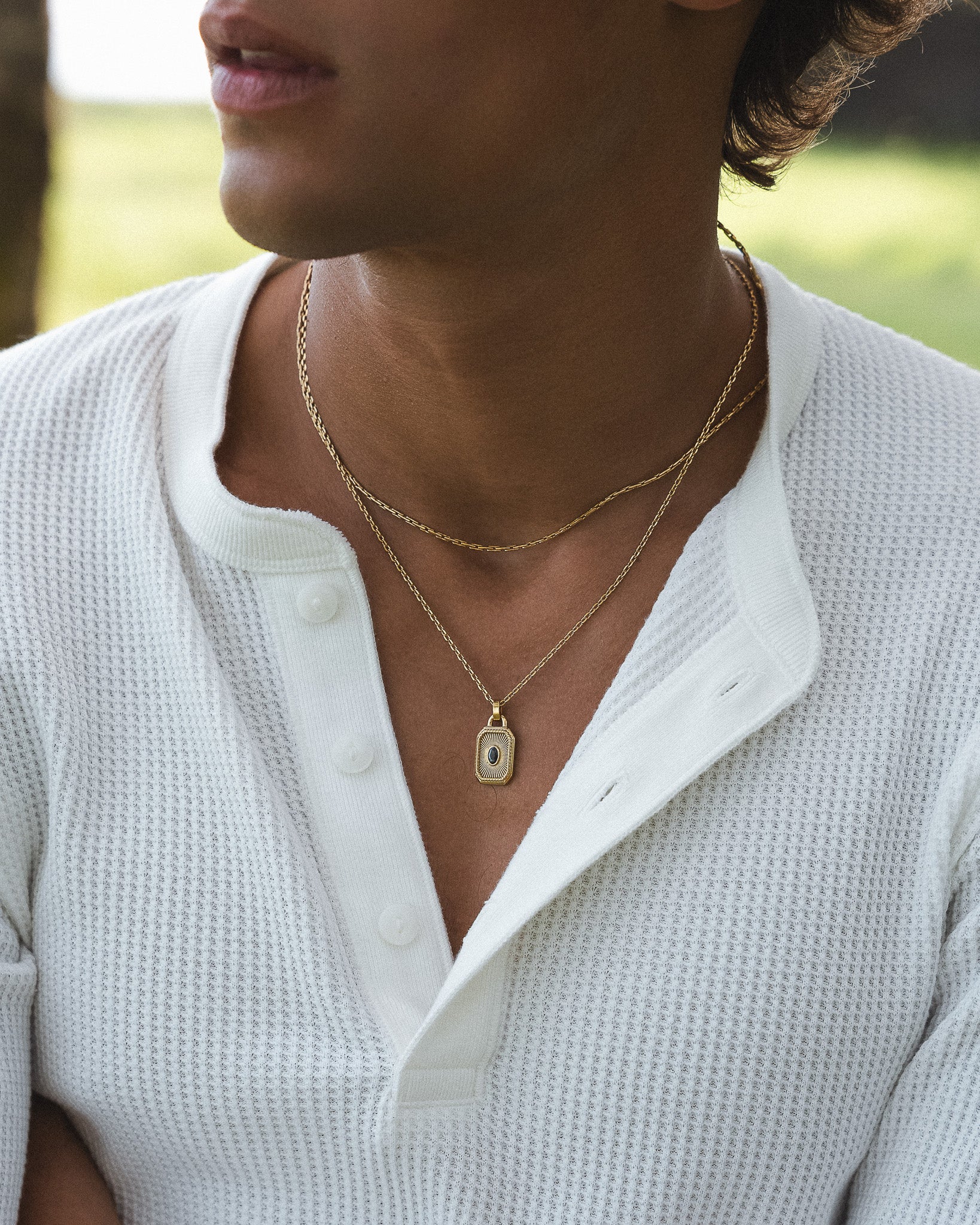 Close up of a person wearing a gold chain necklace around the neck over a white knit top