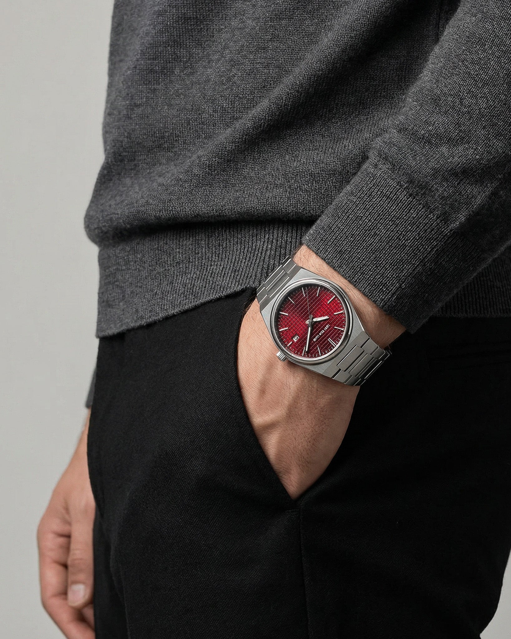 AUREN watch on a wrist with a dark knit sleeve, red dial visible under the cuff.