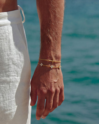 Gold rope chain bracelet on the wrist with a simple chain against a blue water background
