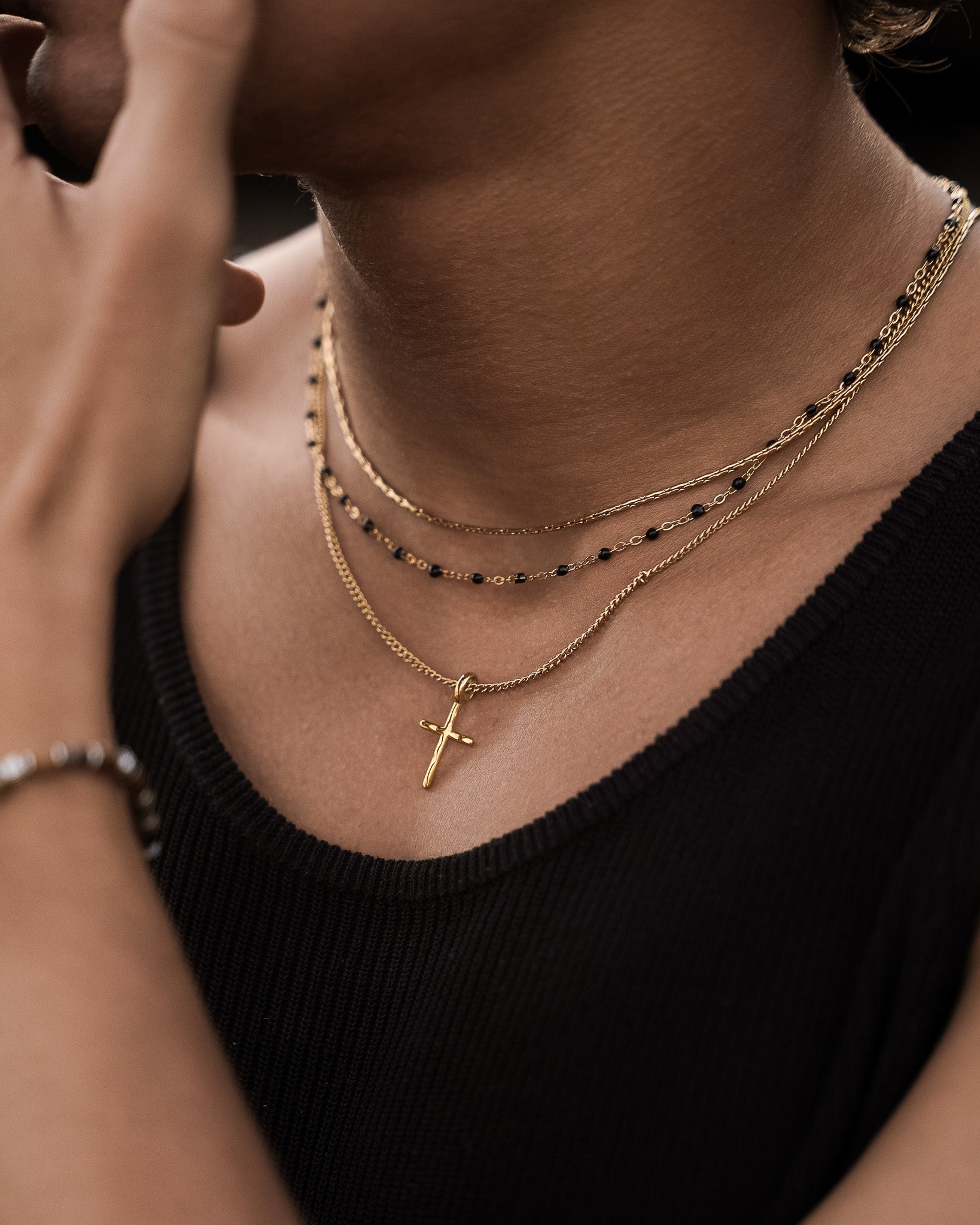 Gold layered chain necklace with a cross pendant on a model's neck