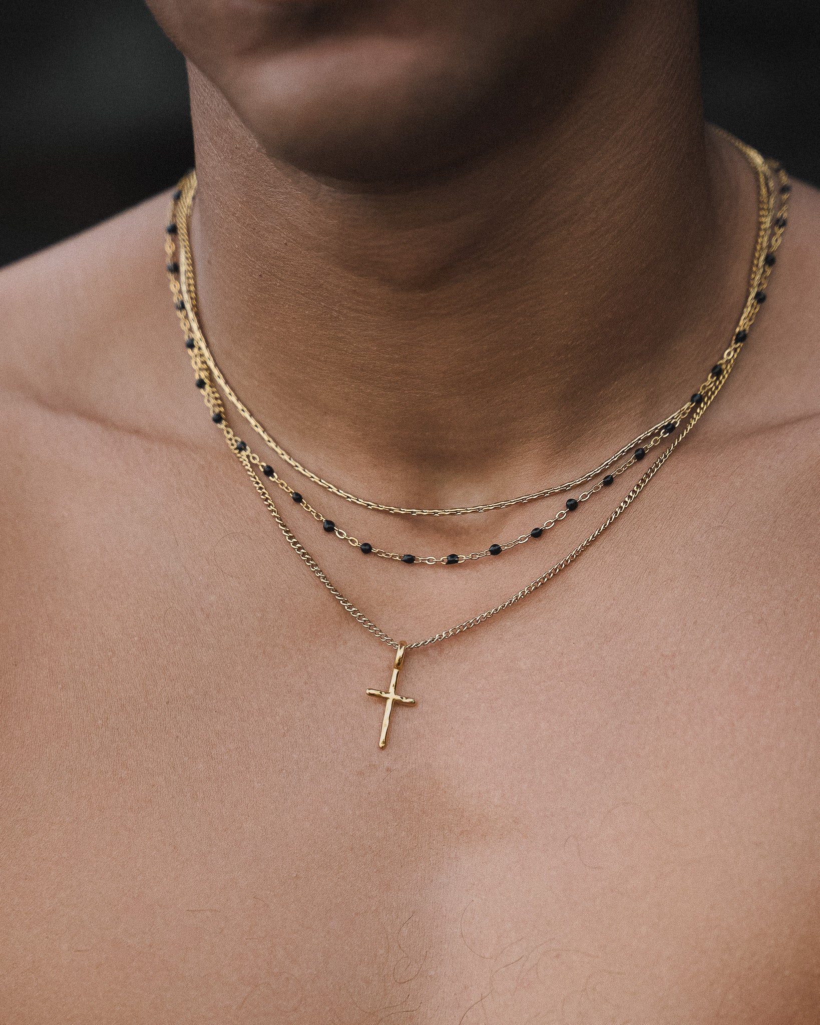 Gold layered necklace with black beads and a cross pendant resting on the chest