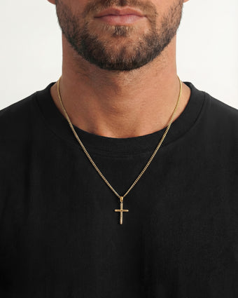 Gold cross pendant on a chain worn by a man in a black shirt.