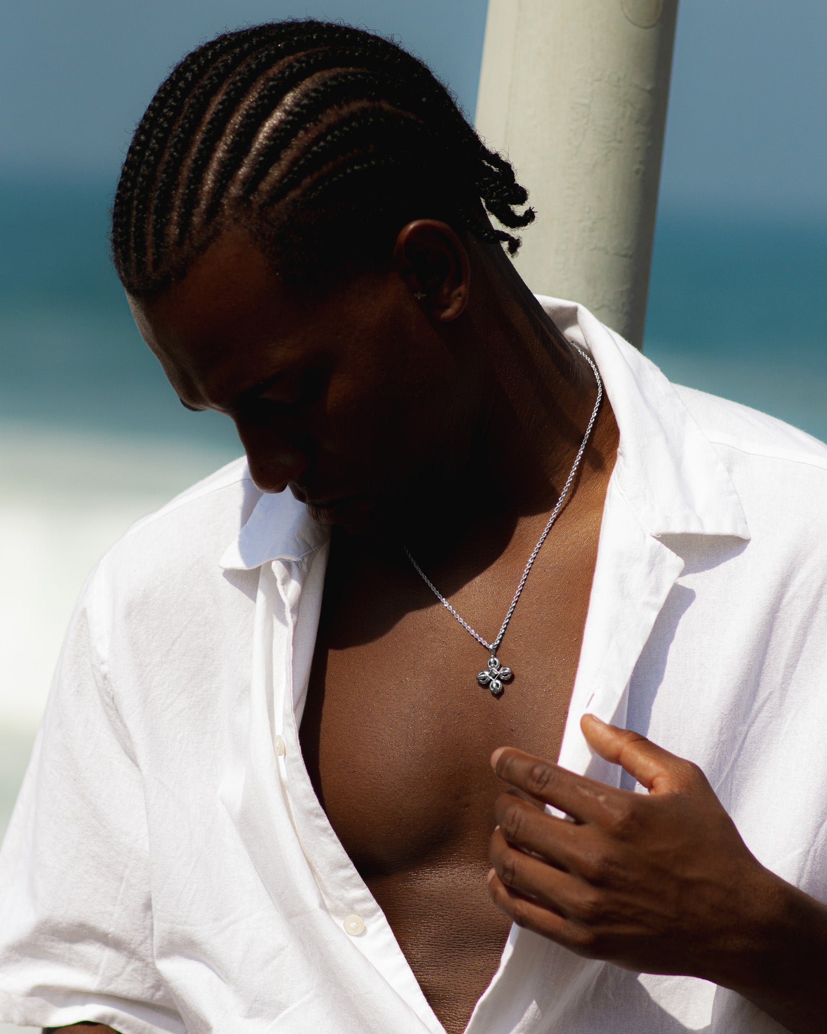 FLARE SILVER NECKLACE pendant shown on chest over white shirt against a seaside backdrop