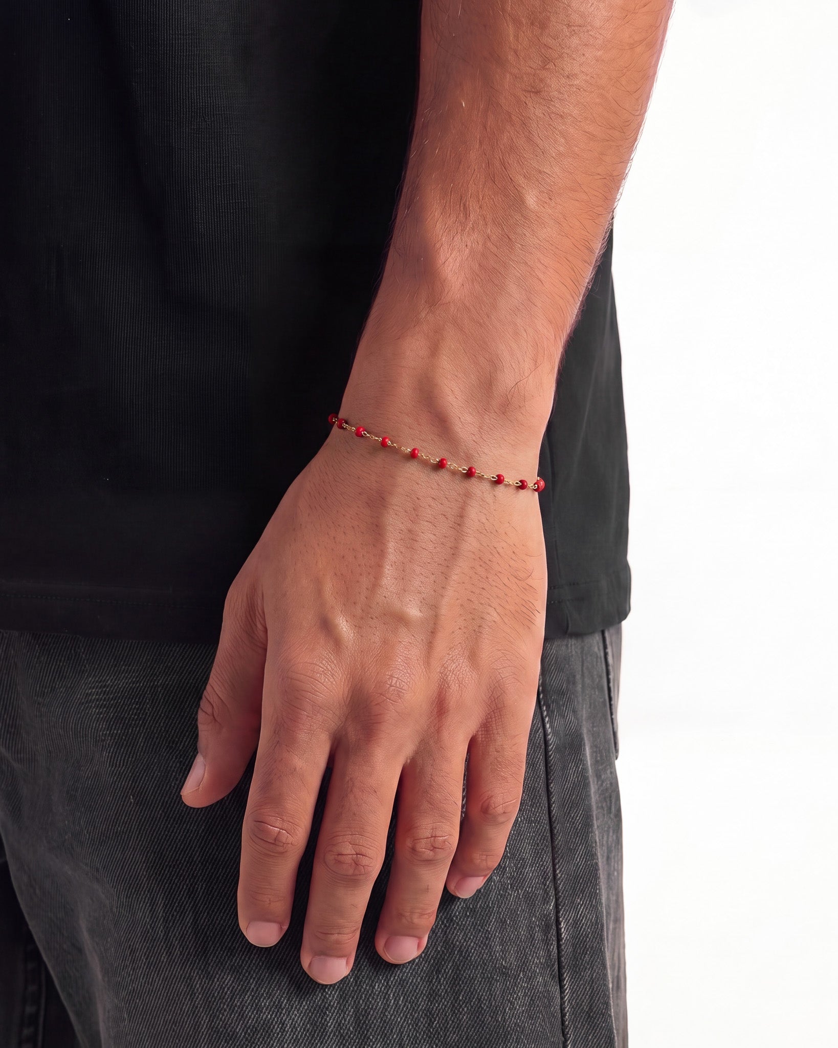 Vista lateral de una pulsera dorada con cuentas rojas en la muñeca