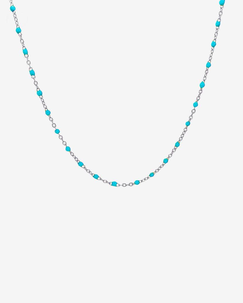 Silver chain necklace with turquoise beads spaced along the links against a light background
