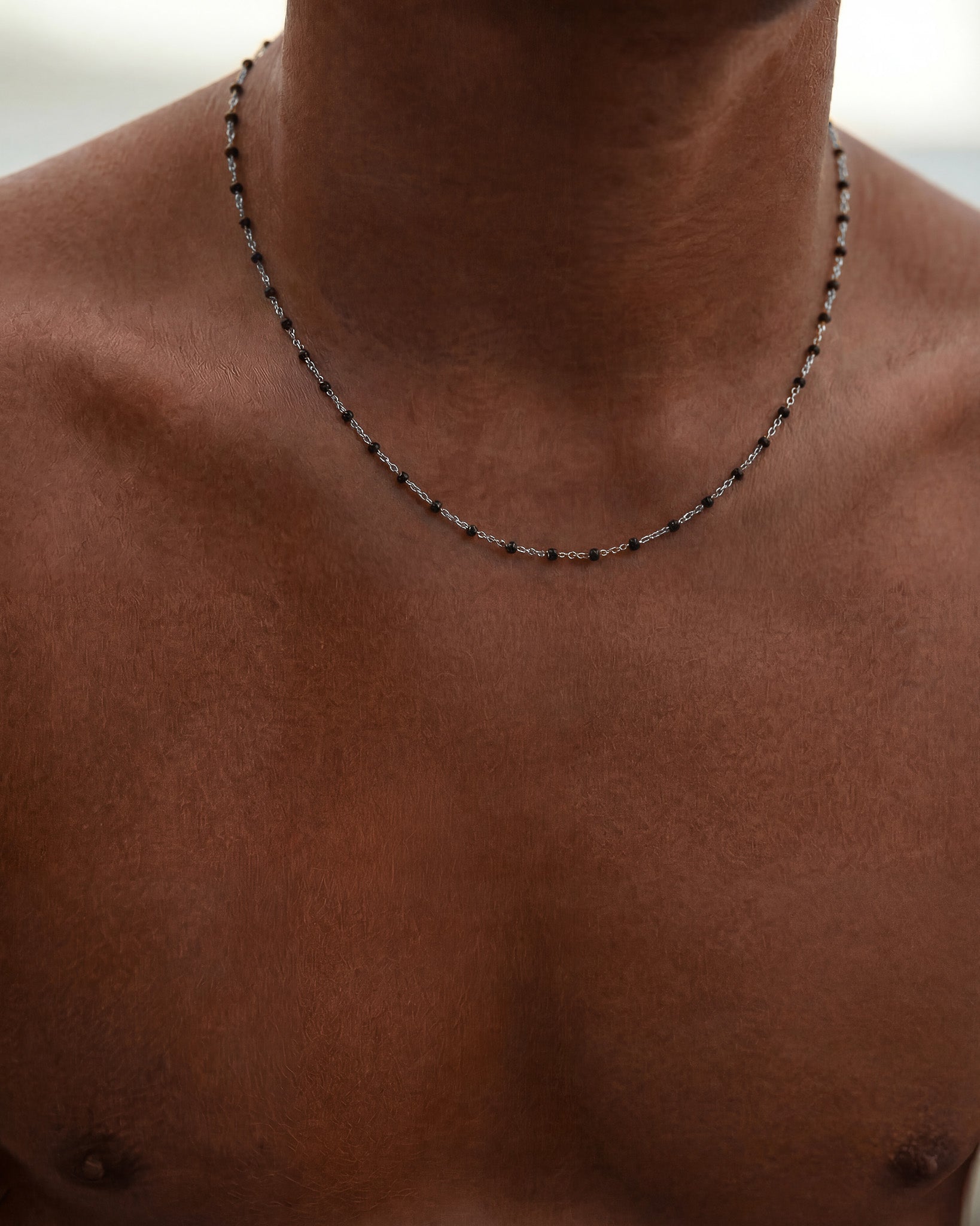 Close up of GEM silver chain necklace with evenly spaced black beads on a dark-skinned neck