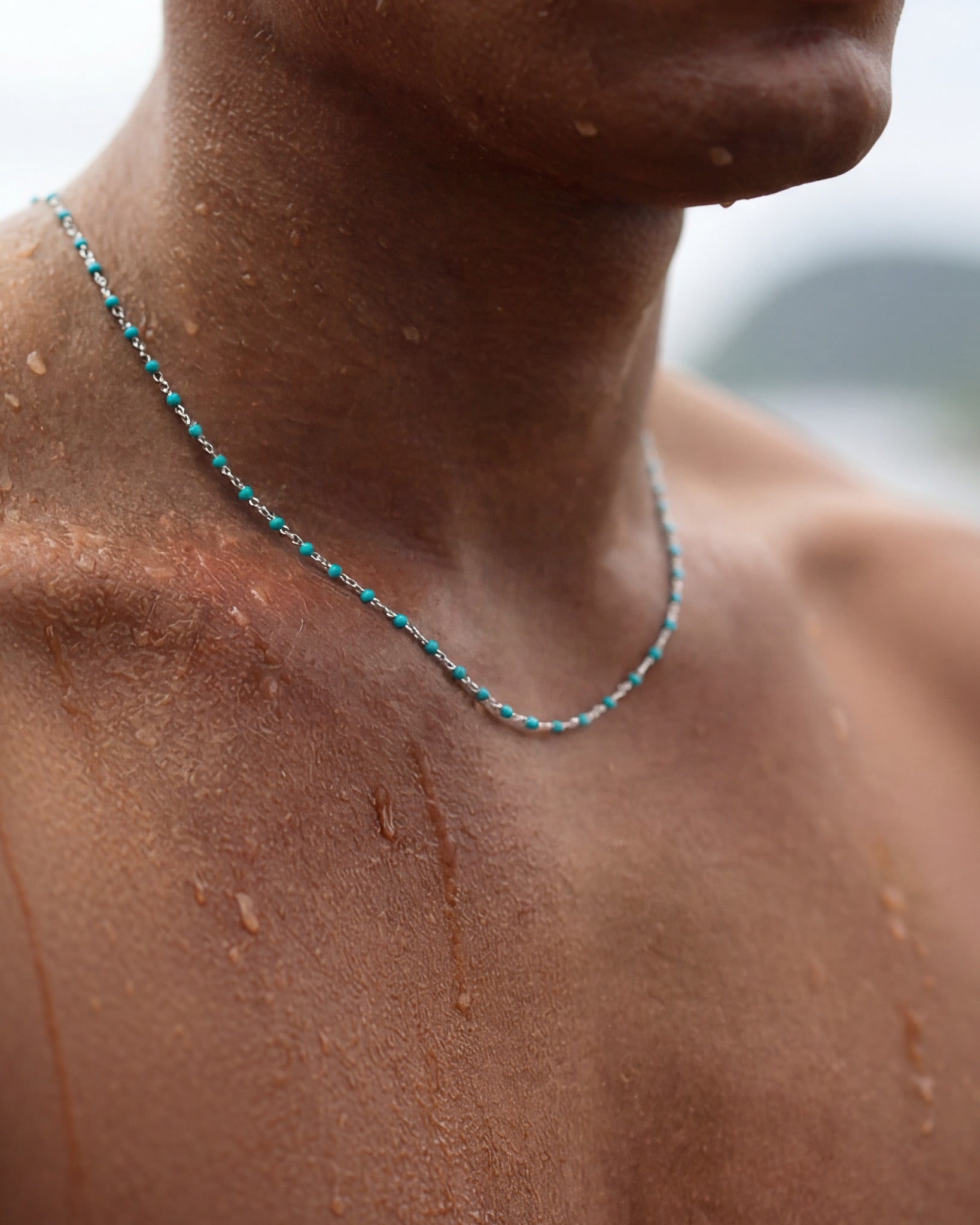 Close-up of turquoise bead silver chain resting on a wet tan neck with water droplets