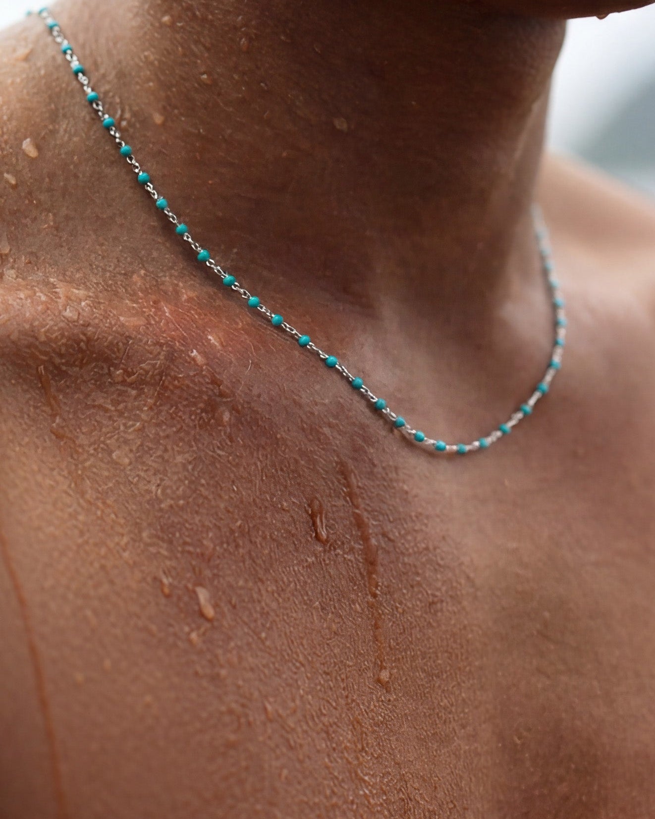 Close-up of turquoise bead silver chain resting on a wet tan neck with water droplets