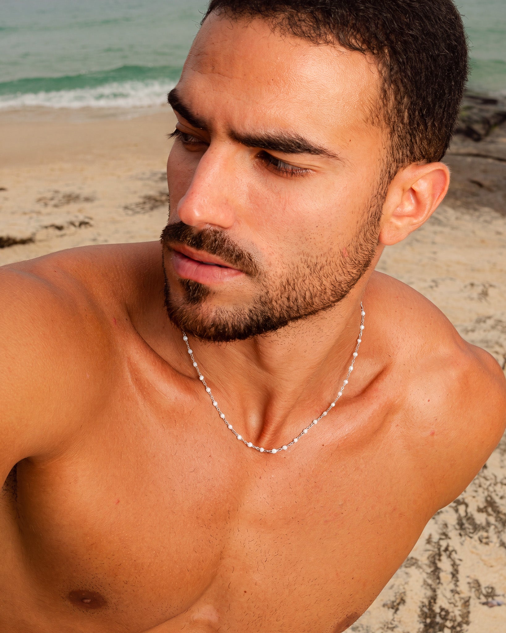 Beaded silver chain necklace with small white beads on a man's chest at the beach