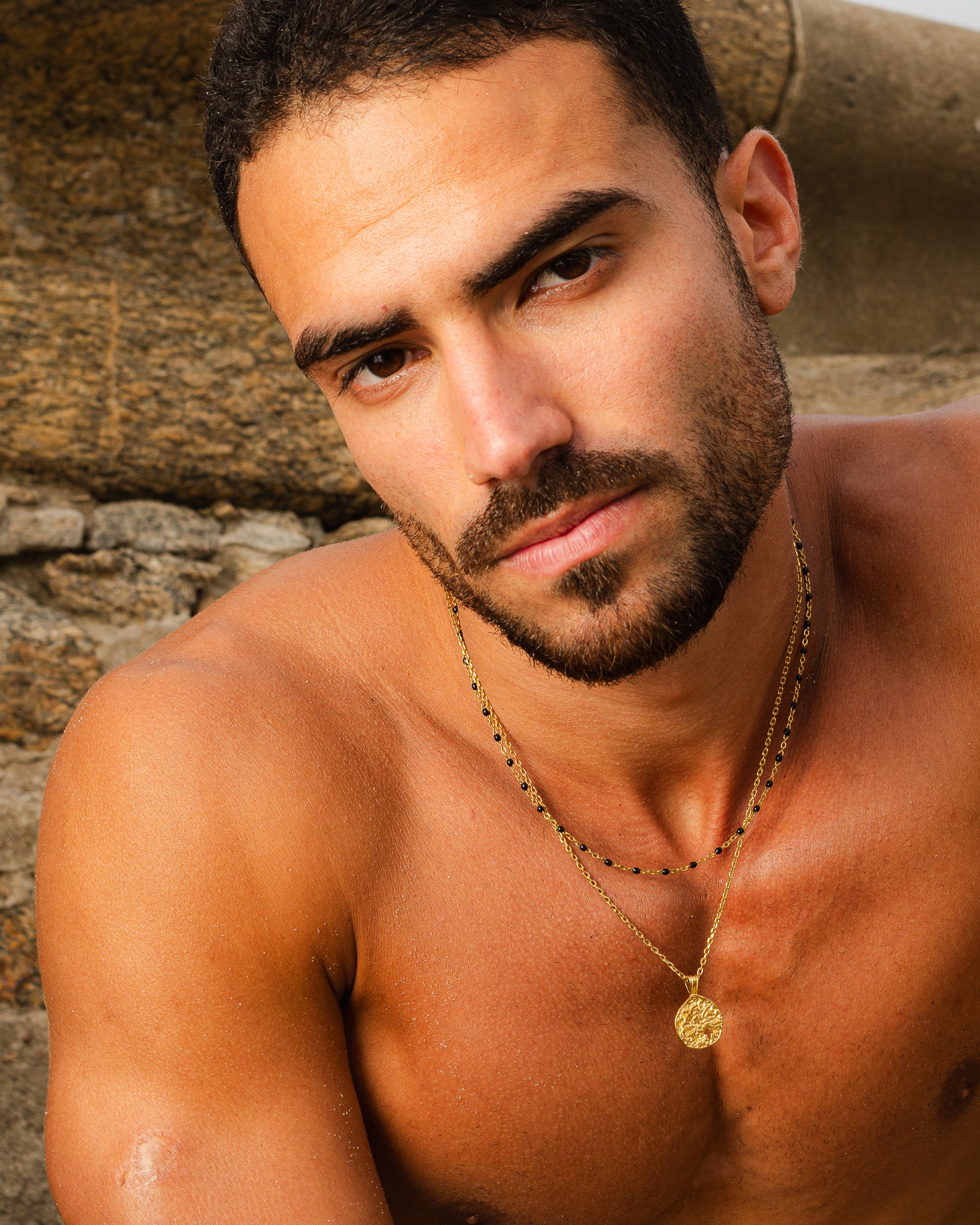 Gold pendant with a textured surface and star cutout on a layered gold chain around the neck
