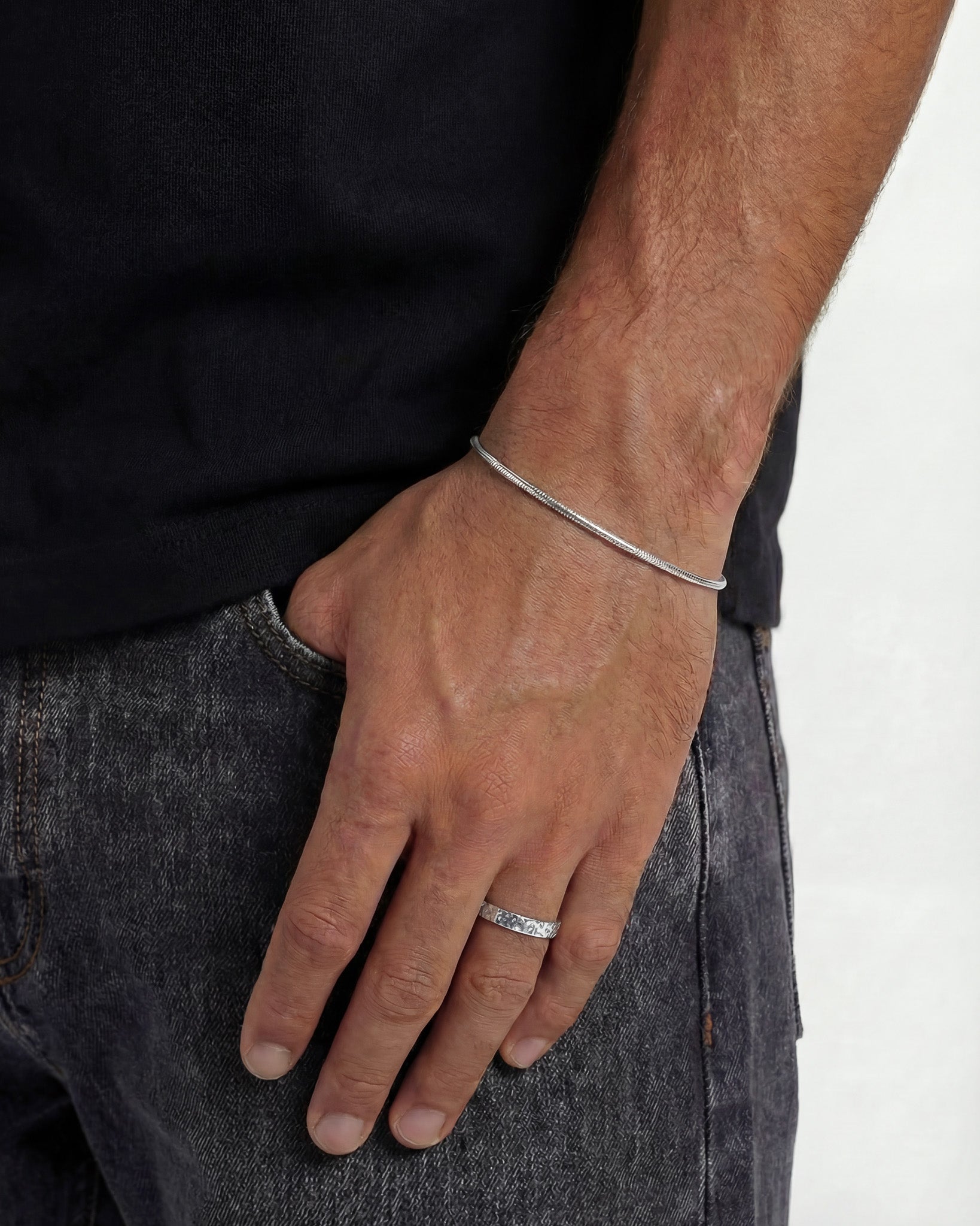 Man wearing a hammered silver ring on the finger with a pendant necklace visible.