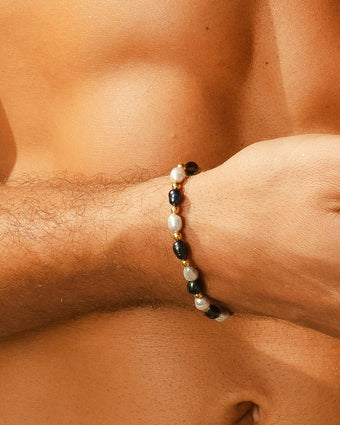 MELASTI Pearl Bracelet on a wrist featuring white pearls dark beads and gold accents with a large pearl centerpiece