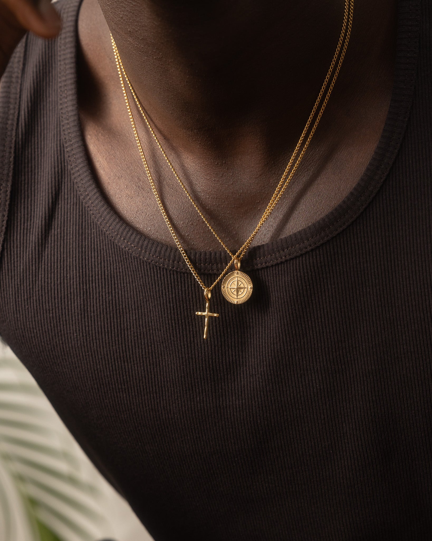 Layered gold necklaces featuring a round medallion pendant and a cross pendant on a black shirt.