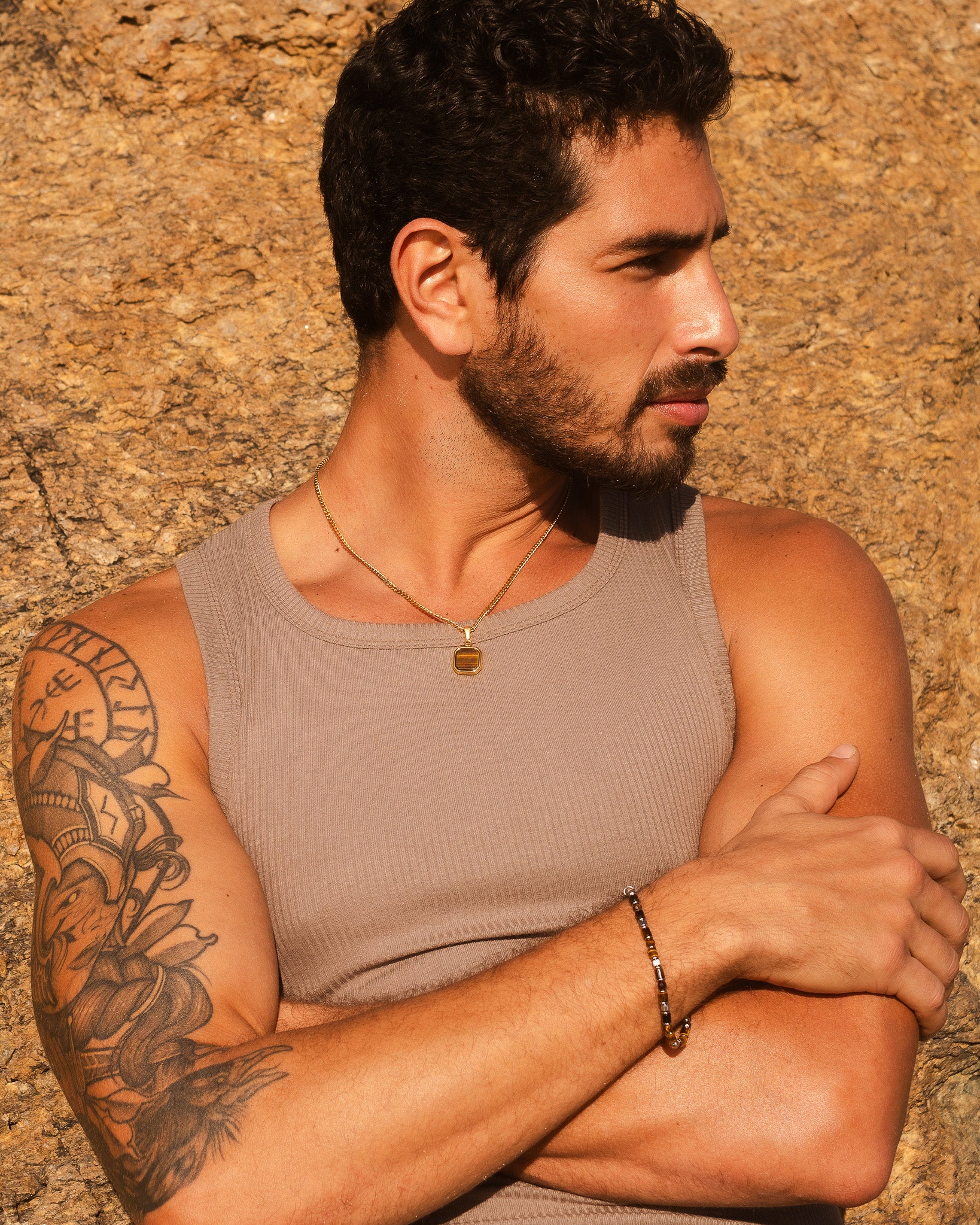 Side profile of a bearded man wearing a gold chain necklace with tiger's eye pendant