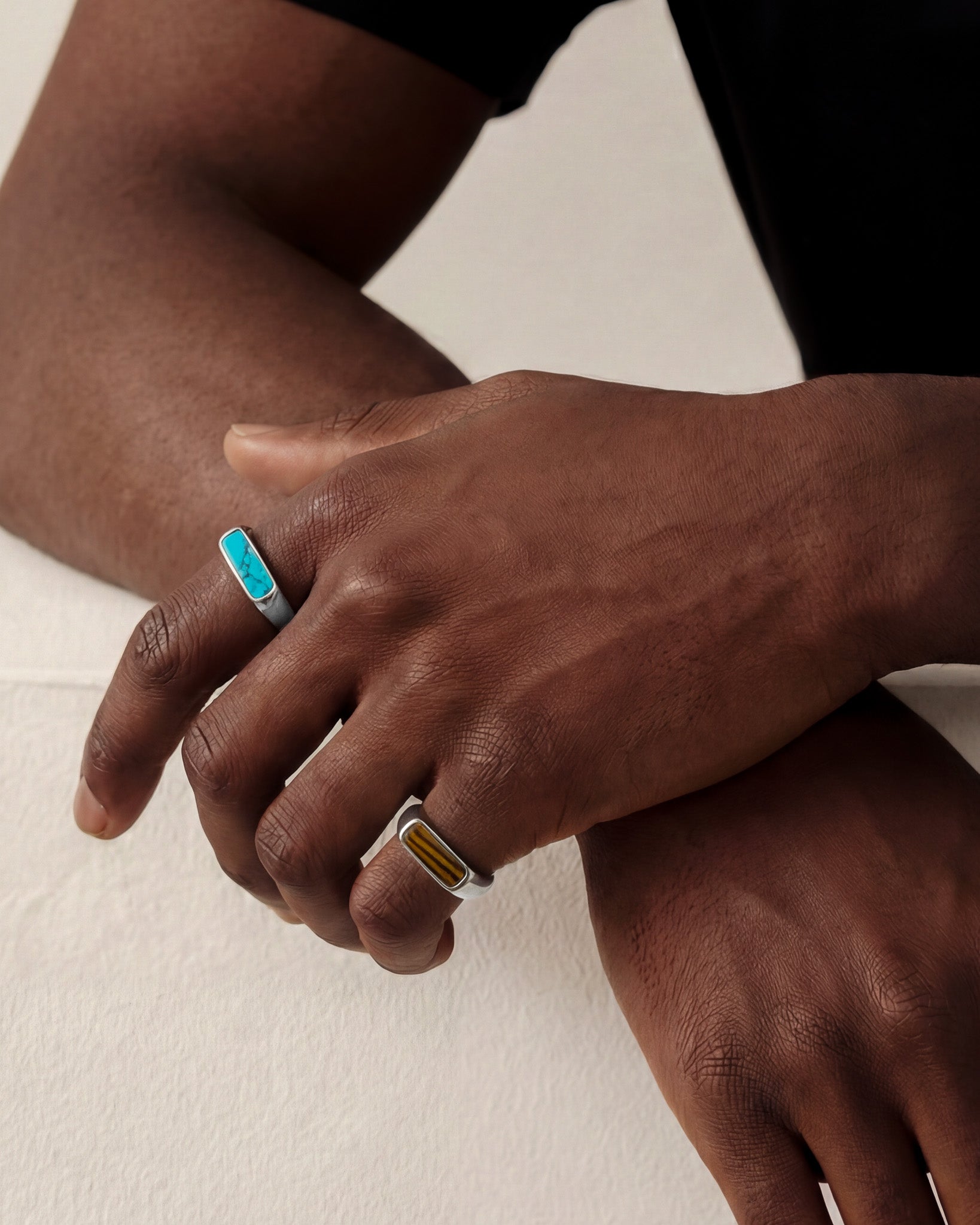 Hand displaying two rings including a NOVA SILVER RING with turquoise inlay and a second amber stone ring