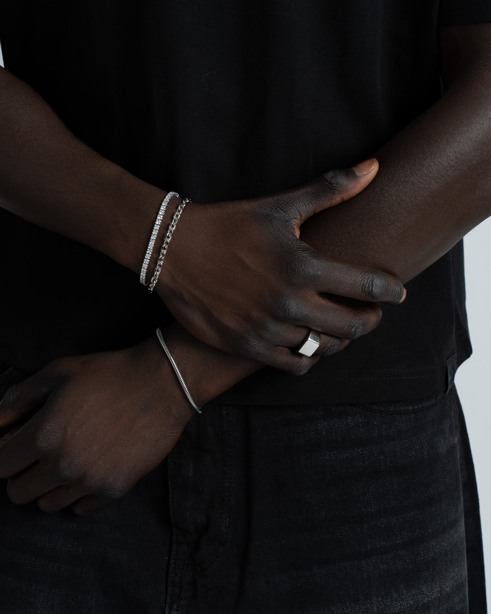 Two silver bracelets on a dark-skinned wrist; an anchor link bracelet and a pavé diamond chain against a black top