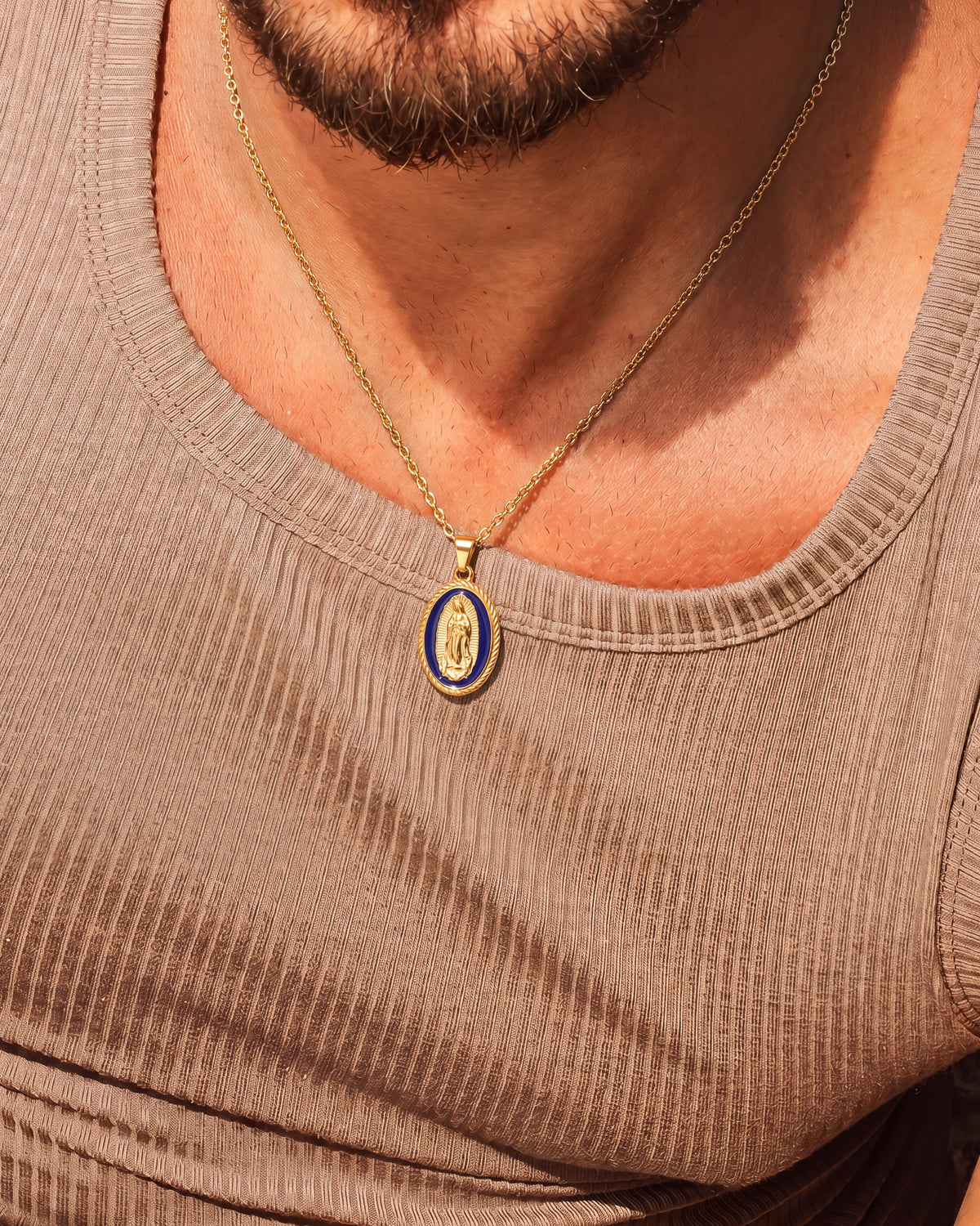 Collar dorado de la Virgen María sobre top de punto topo con colgante ovalado de esmalte azul
