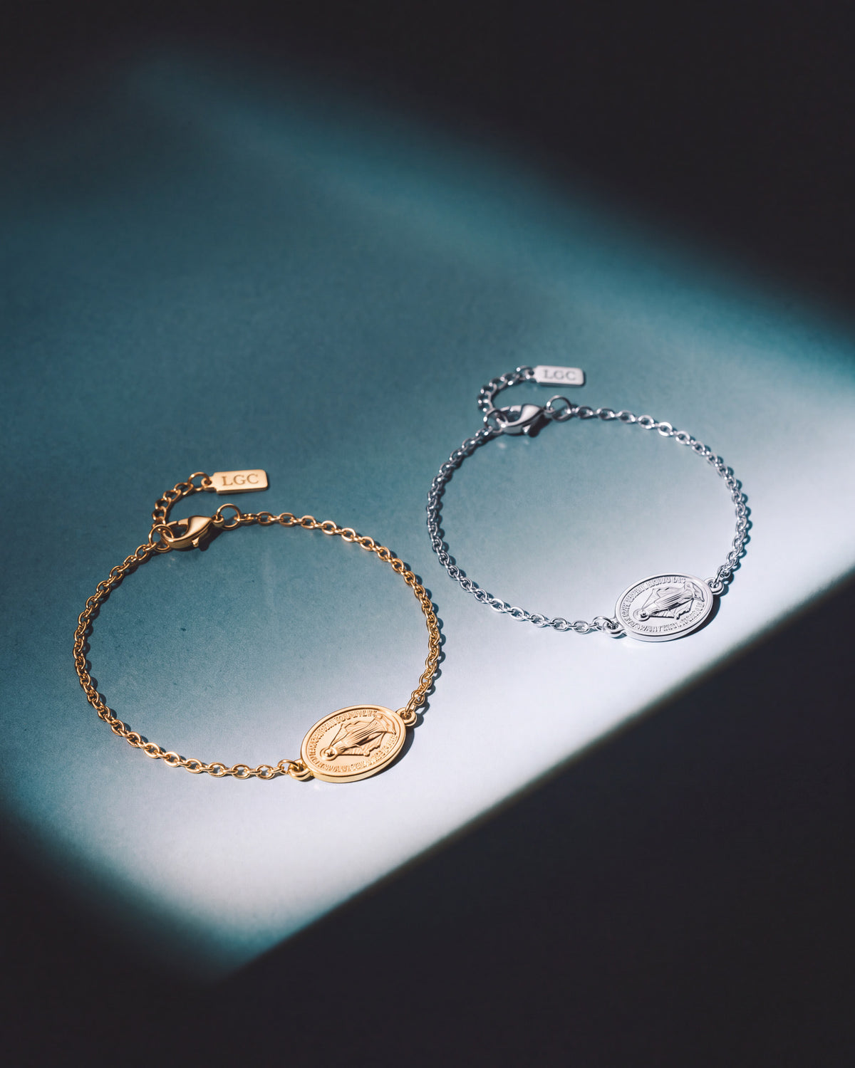 Gold and silver chain bracelets with coin charms displayed on teal background.