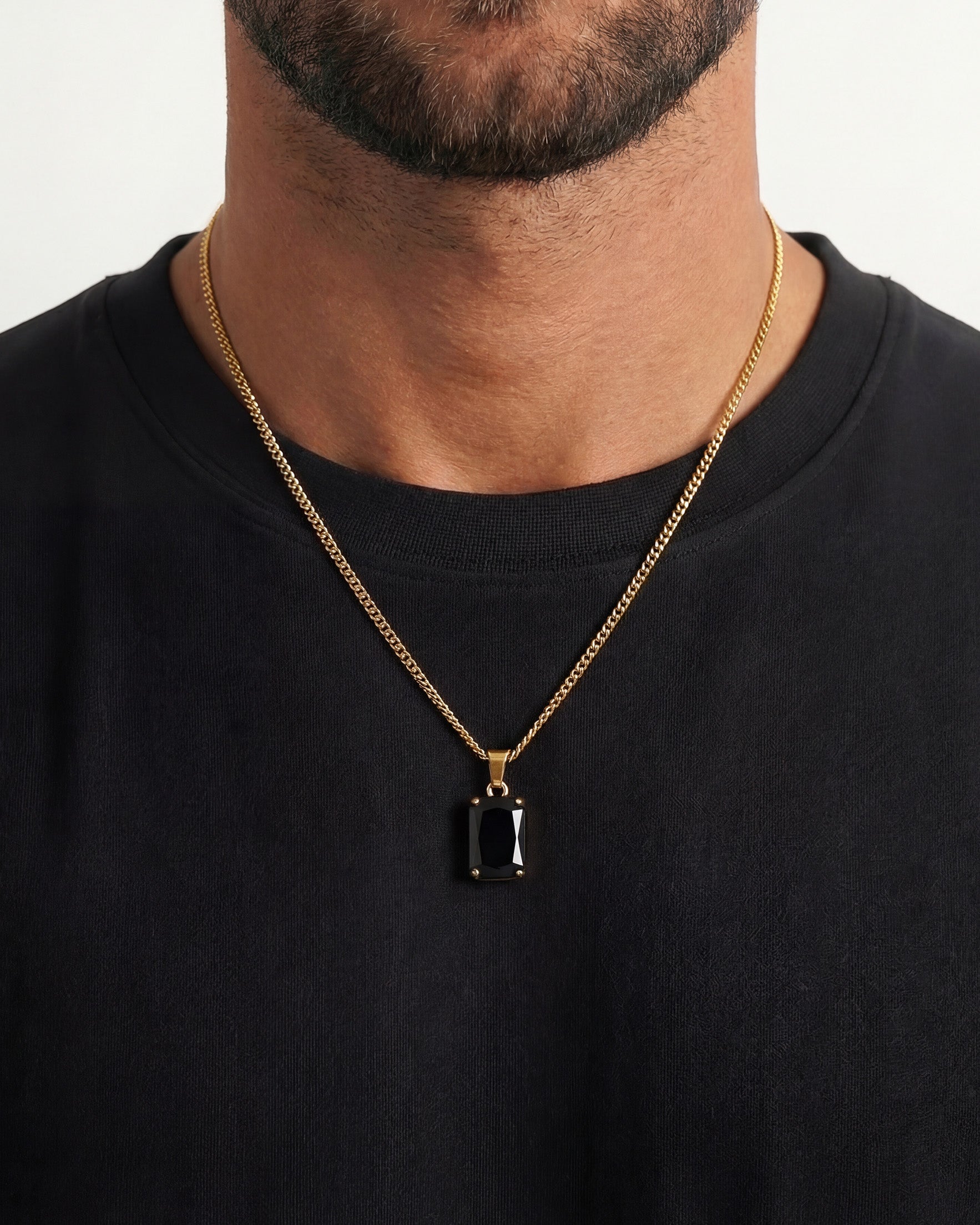 Close up of a person wearing a gold chain necklace with a black rectangular pendant on a black shirt