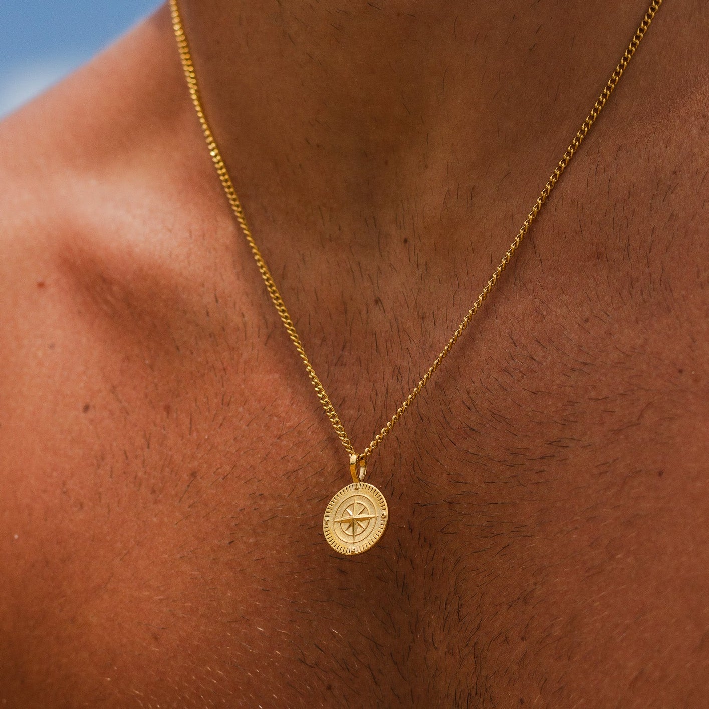 Gold chain necklace with a round compass pendant resting on a man's chest