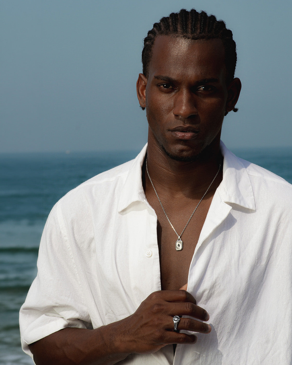 Man by the sea wearing a Helio silver ring and a pendant necklace