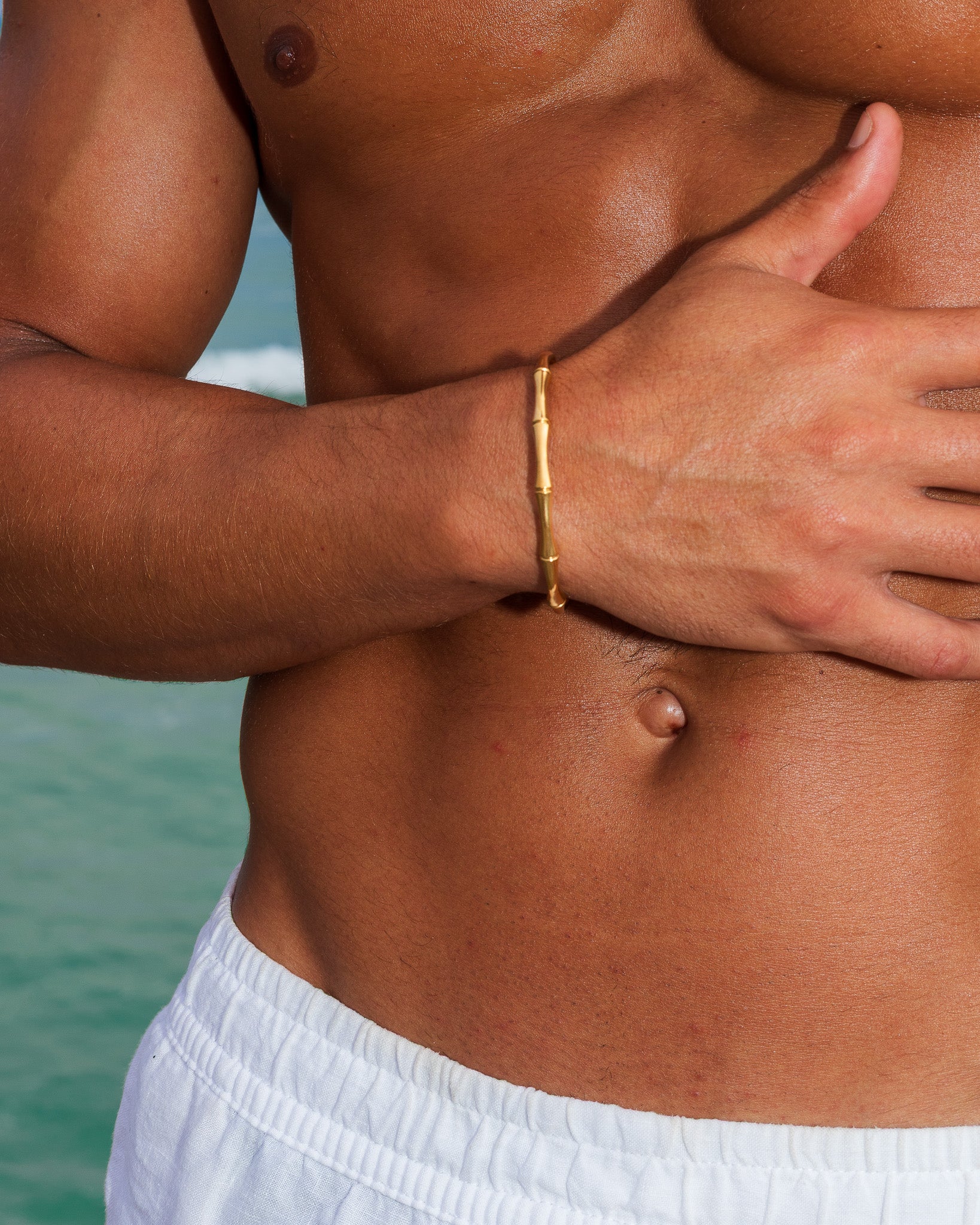 Gold bamboo bracelet on a wrist shown against the sea and sky background.