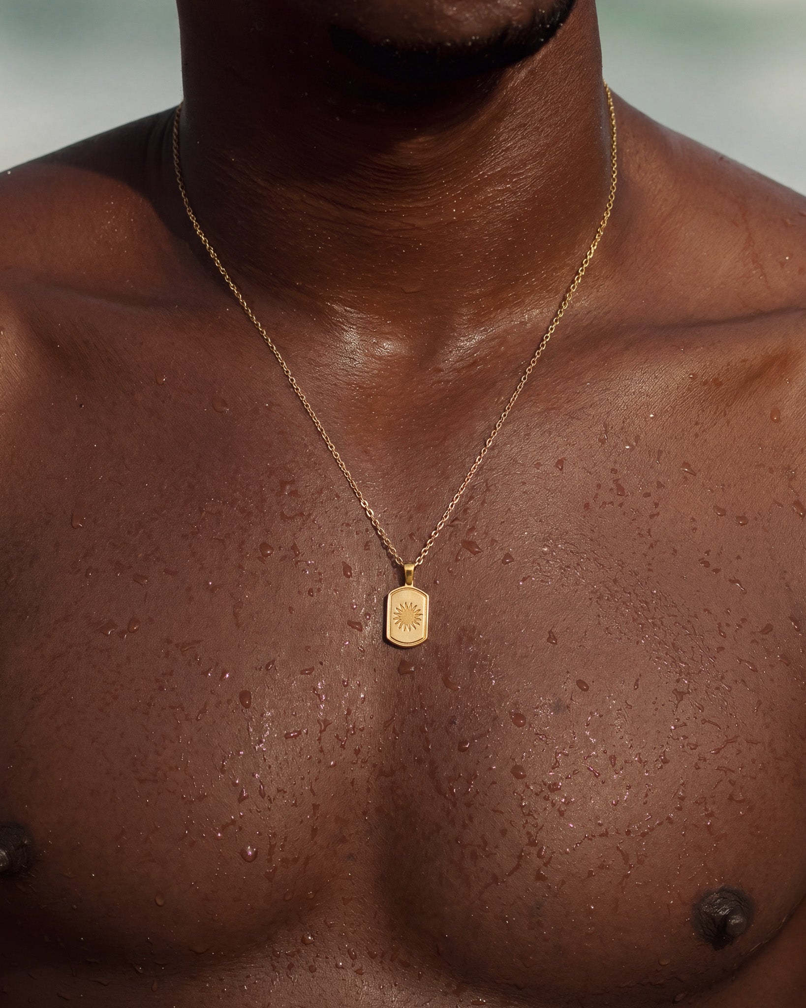 DAYSTAR gold necklace worn on dark skin with a rectangular sunburst pendant
