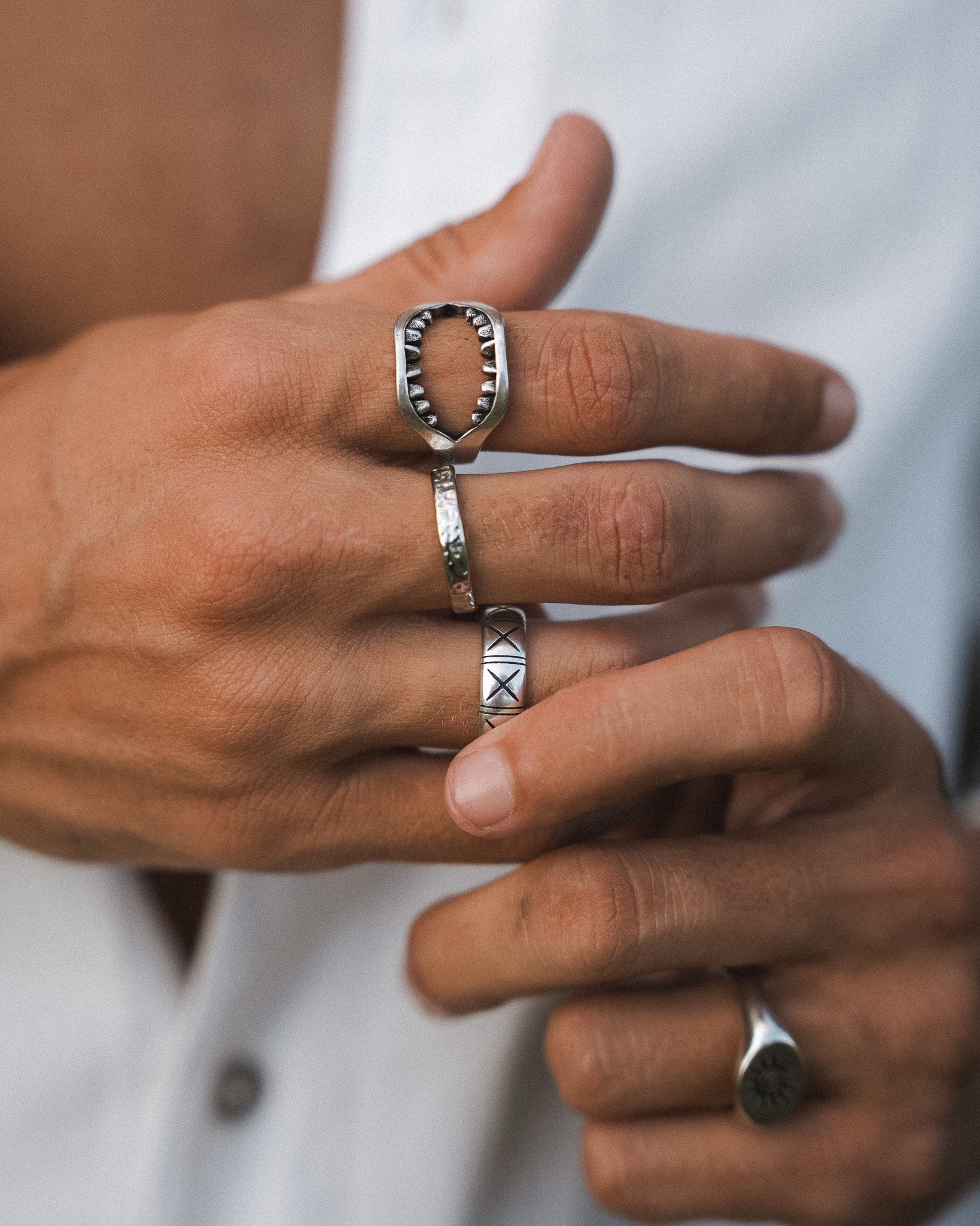 Close up of a hand wearing a square silver ring with toothlike inner edges.