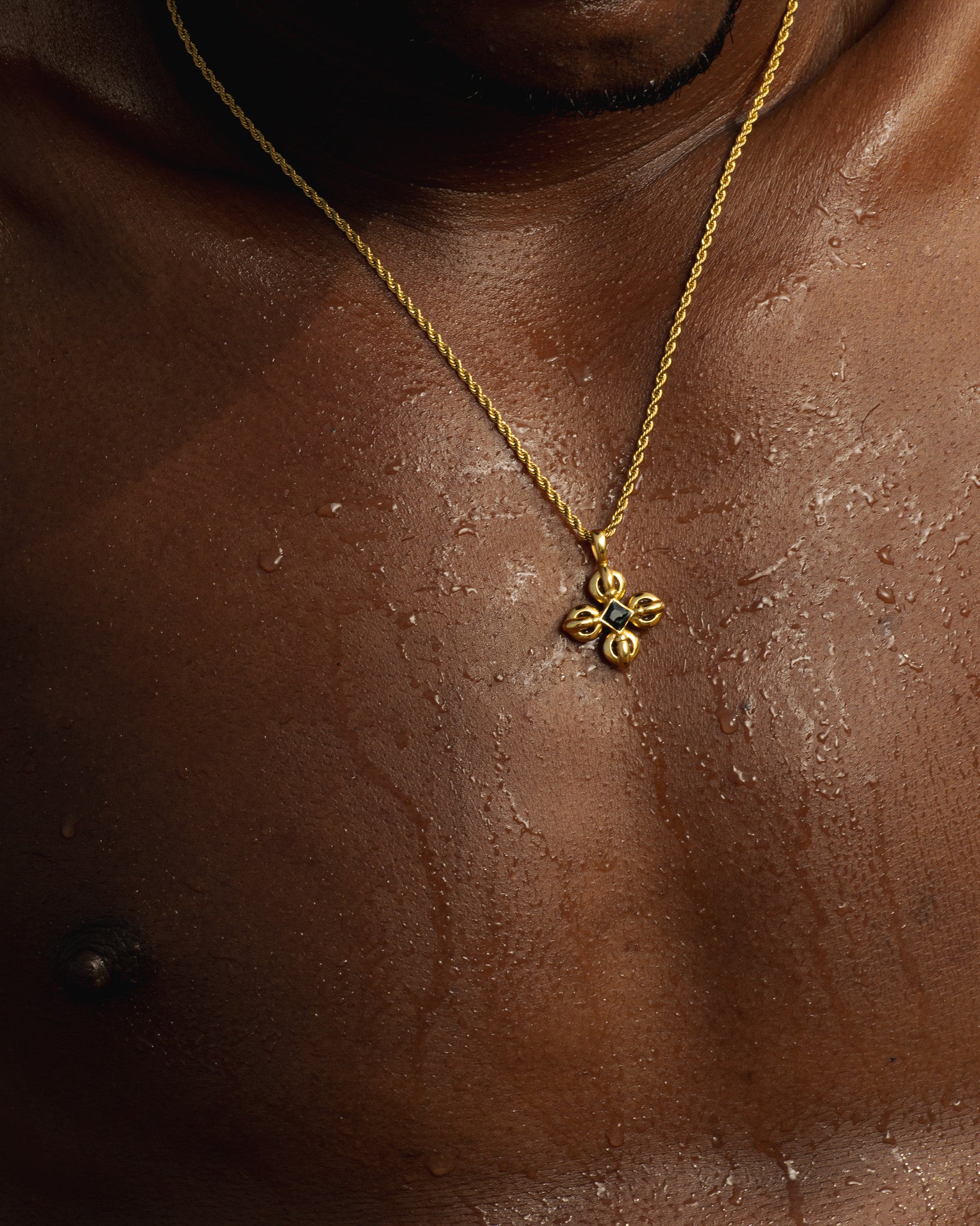 Gold chain necklace with ornate cross pendant featuring a dark center stone on the model's chest.