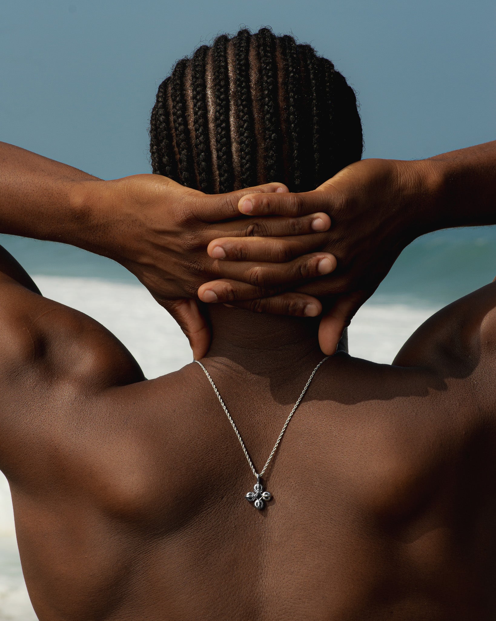 FLARE SILVER NECKLACE chain around neck with pendant resting on the chest back view of model on the beach