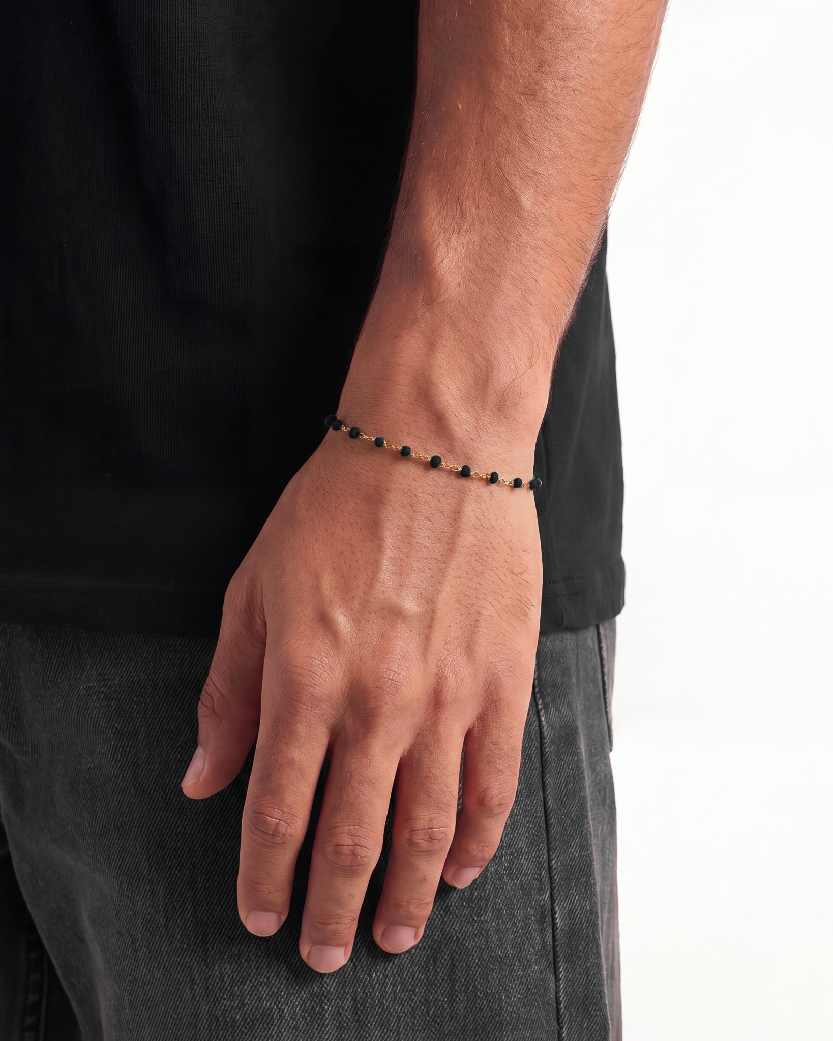Gold chain bracelet with small dark beads worn on the wrist