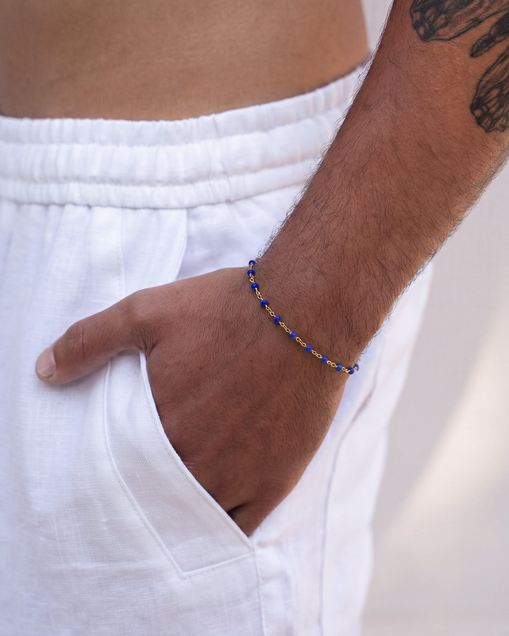 Gold bracelet with blue beads on a wrist against white fabric