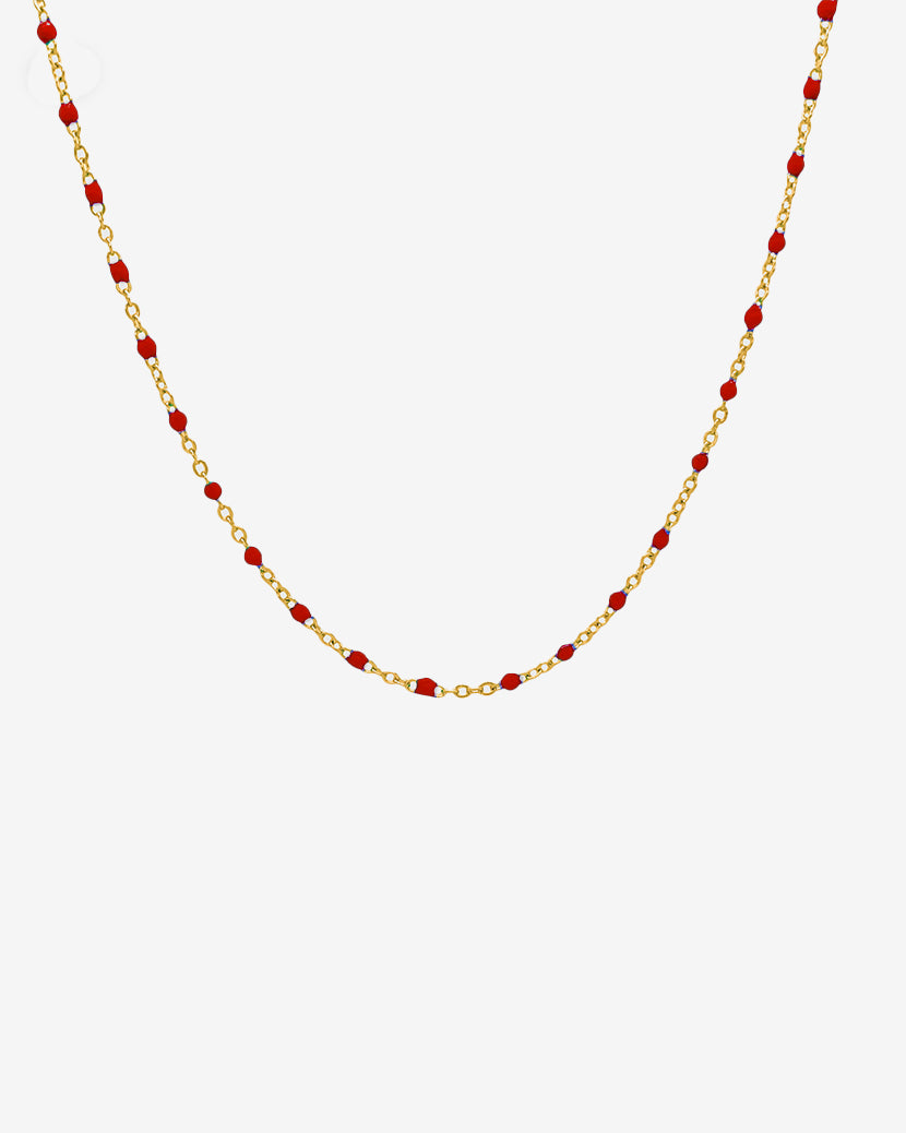 Delicate gold chain necklace with evenly spaced red beads against a white background