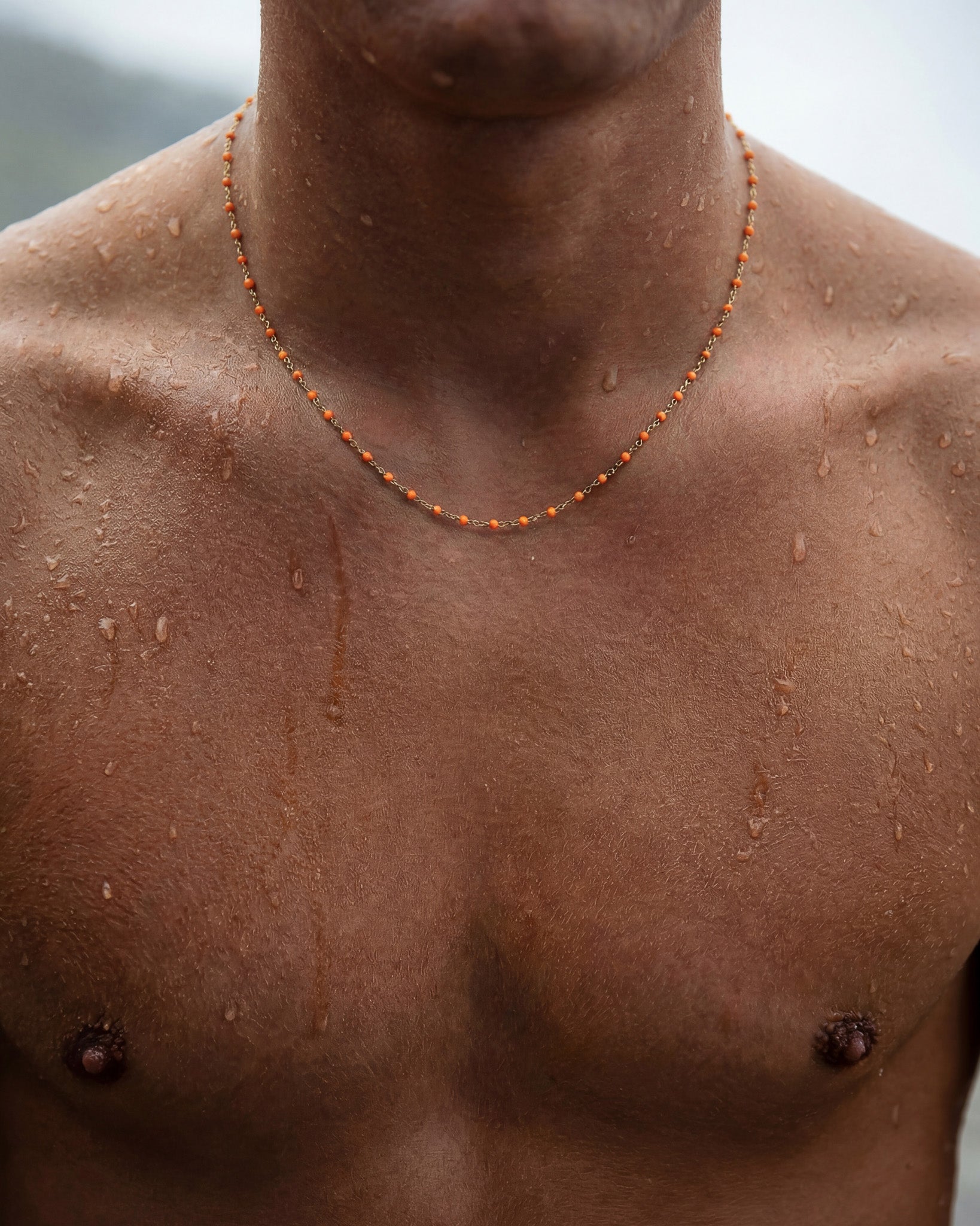 GEM GOLD CHAIN necklace with orange beads worn around a dark-skinned model's neck.