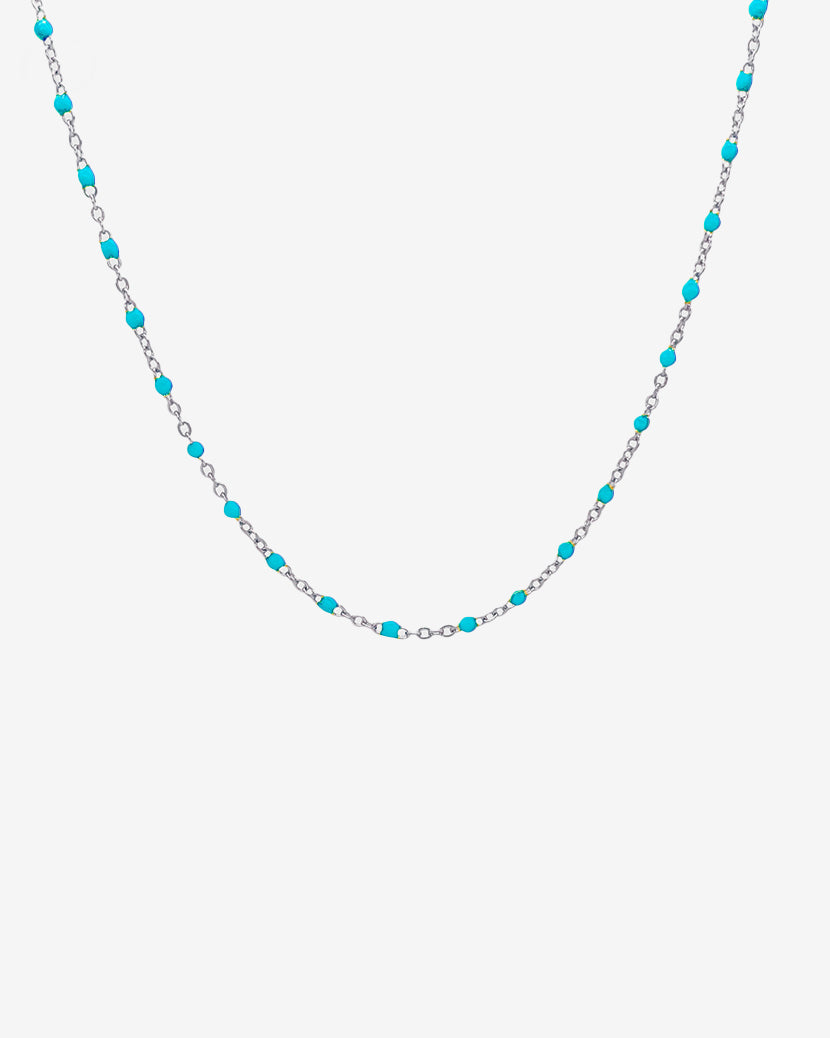 Silver chain necklace with turquoise beads spaced along the links against a light background
