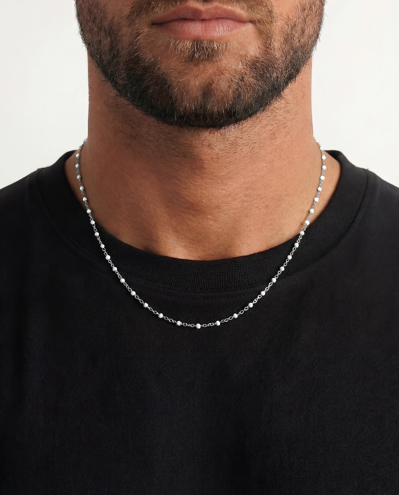 Close up of a man wearing a silver beaded chain necklace around the neck