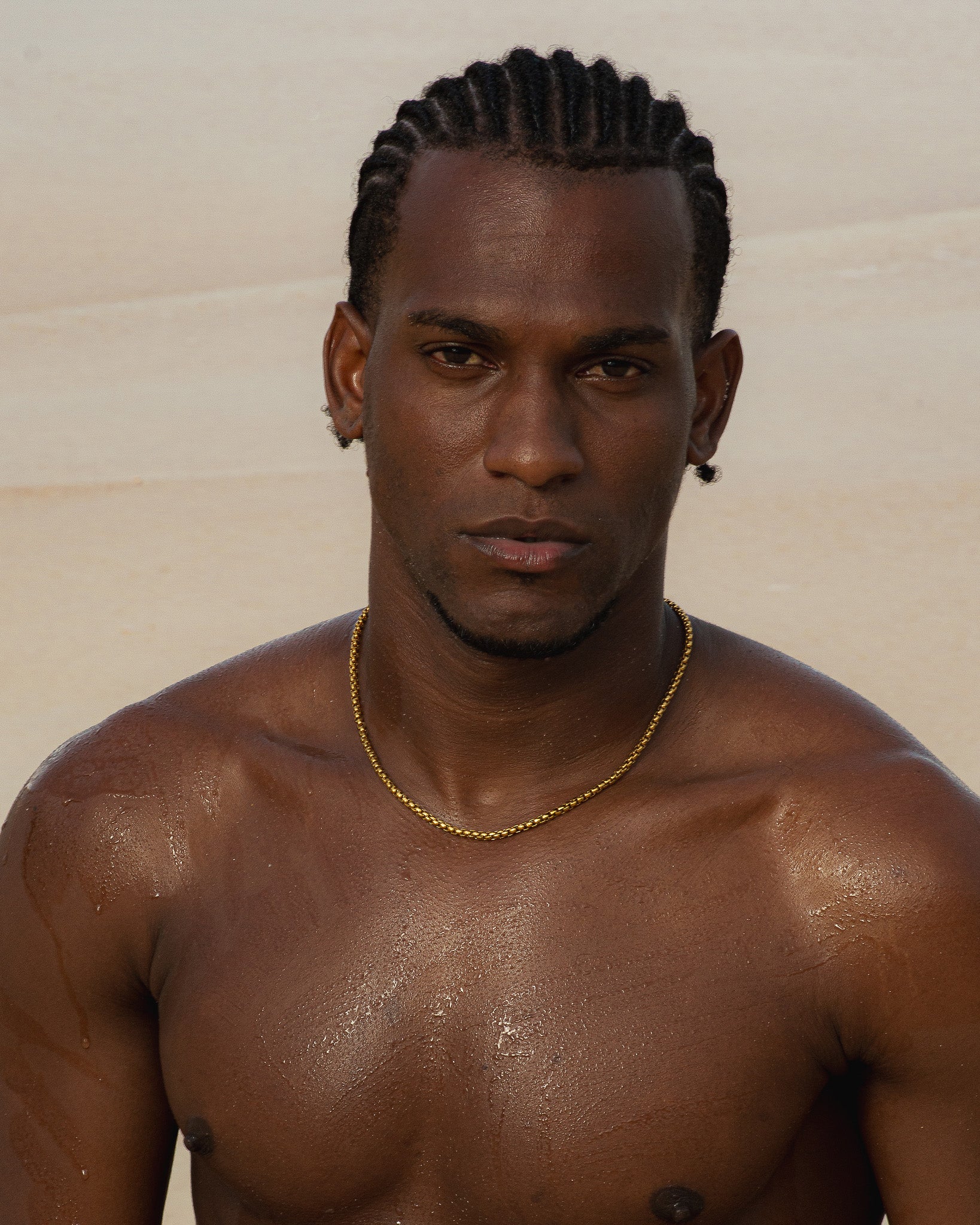 Close up of NOIR gold chain resting on a shirtless man at the beach