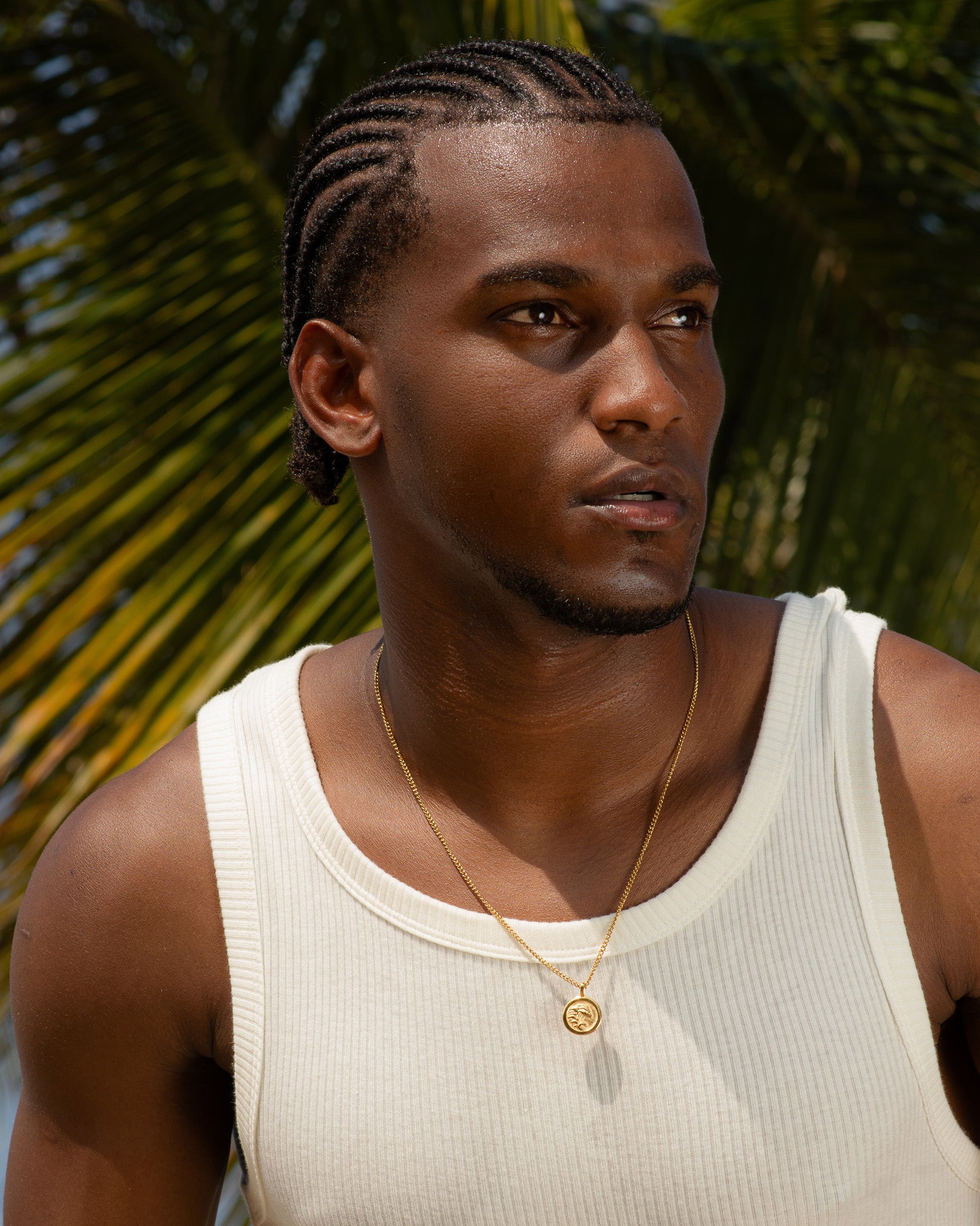 Gold coin pendant necklace on a man wearing a white ribbed tank top, pendant resting at the chest.