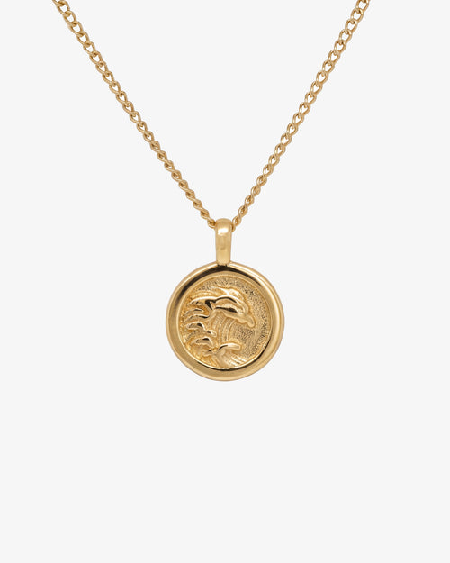 Gold OAHU necklace with a round palm tree pendant on a pale background