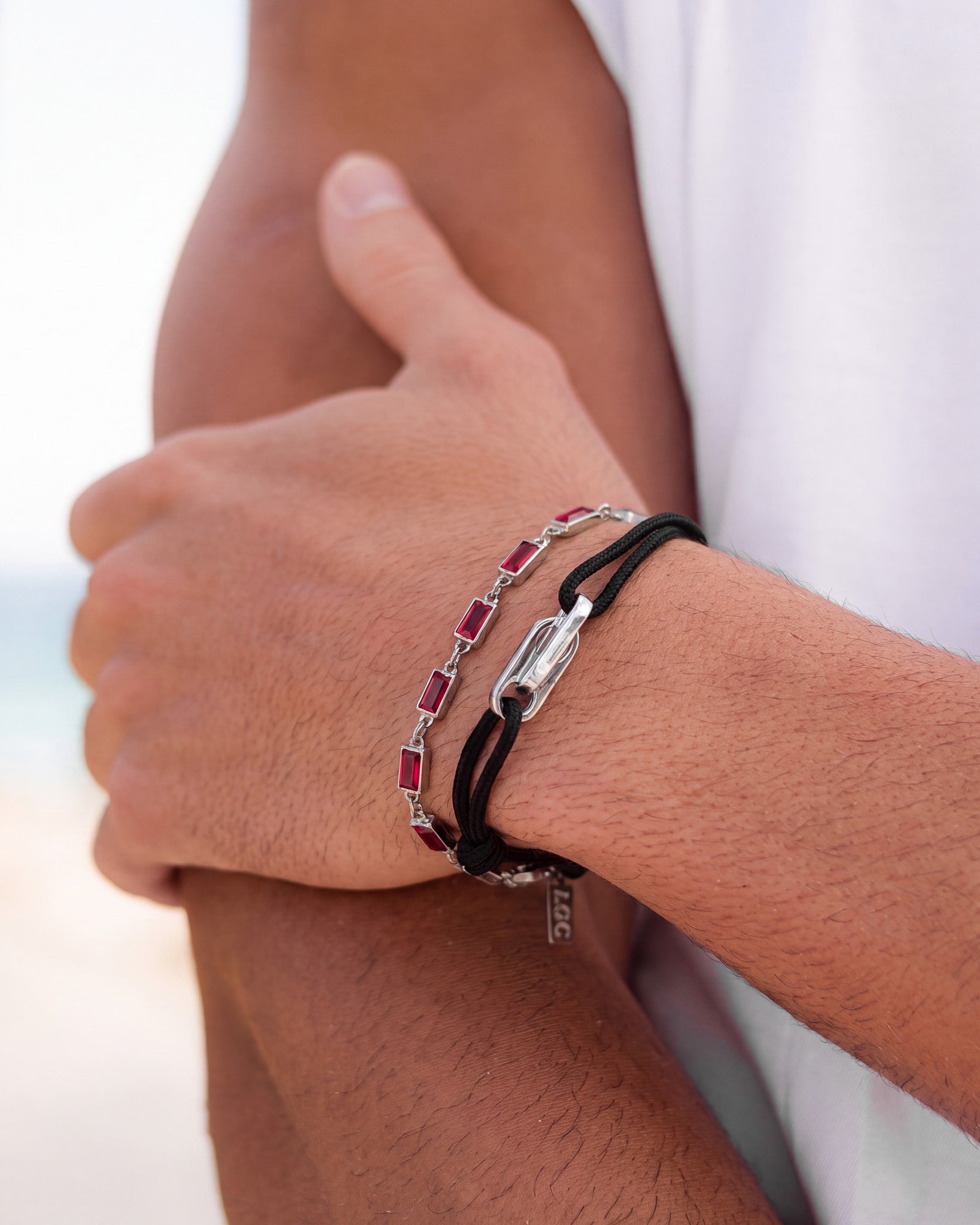 Primer plano de una muñeca con una pulsera de gemas rojas combinada con una pulsera de cordón negro