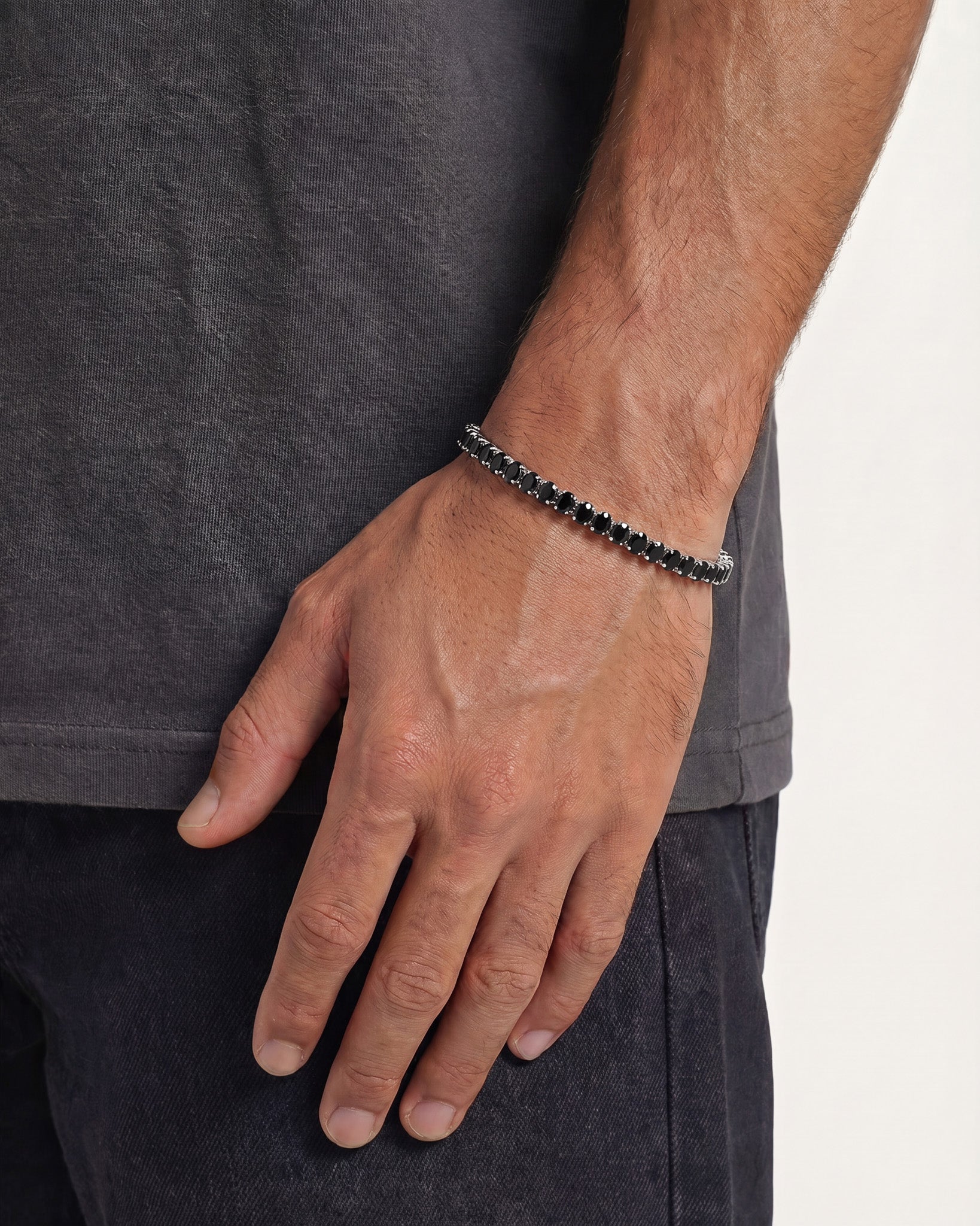 Pulsera tennis plateada ovalada con piedras negras en la muñeca de un hombre